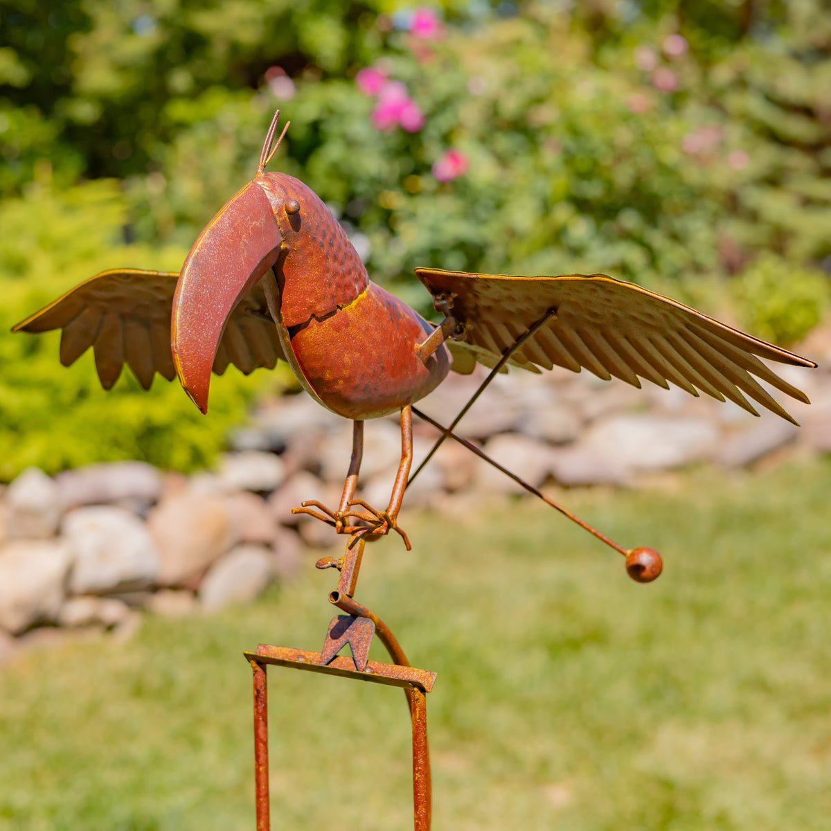 Close view of a rust-finish toucan stake with wide wings in a green garden