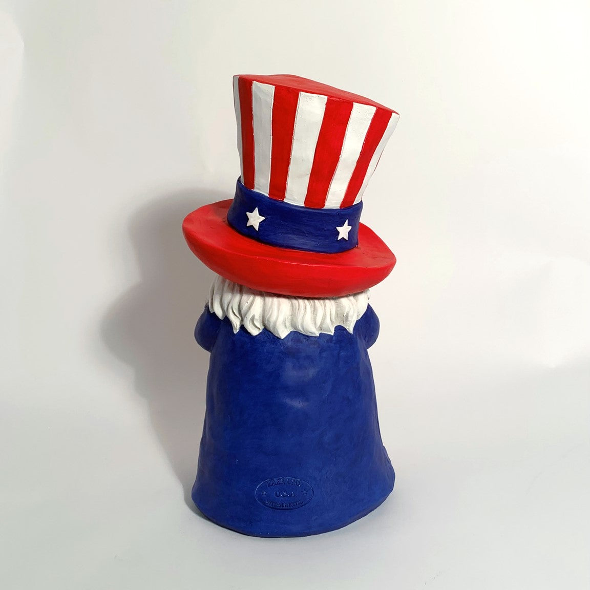 Rear view of a blue gnome wearing a red and white striped hat against a light backdrop