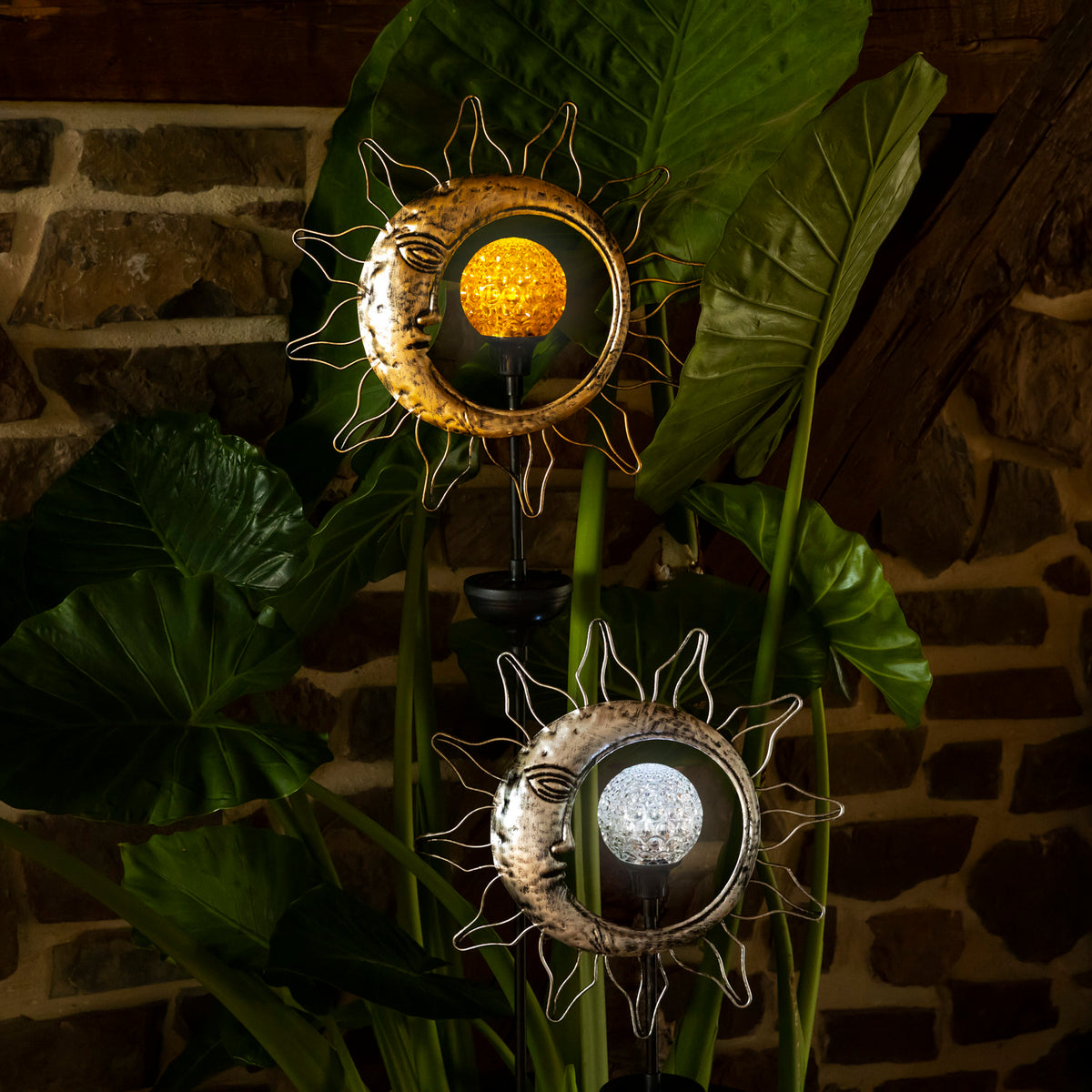 Gold and silver sun-and-moon stakes glow among broad leaves against a stone wall in dim light.
