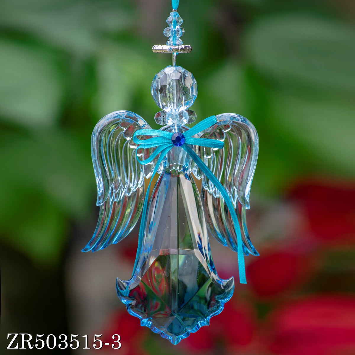A clear hanging angel ornament with layered wings and a turquoise bow, shown against a soft garden background.