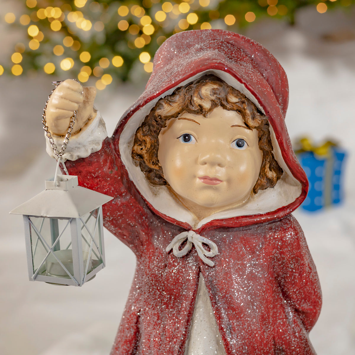 Close view of a hooded figure in a red cloak holding a hanging lantern by its chain.