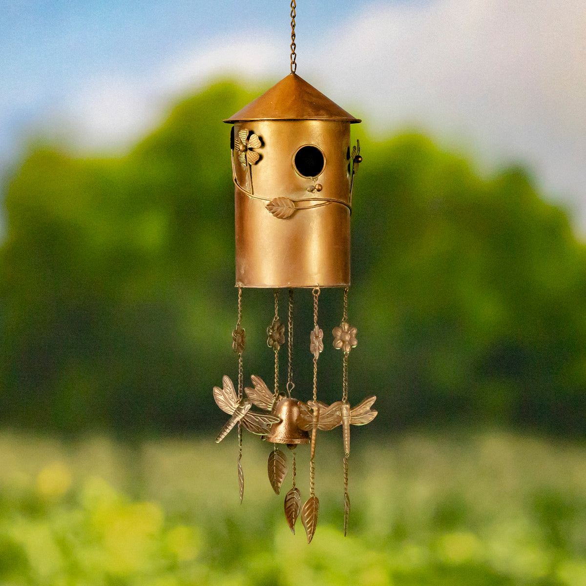 Copper-toned birdhouse wind chime hanging against a softly blurred green garden background