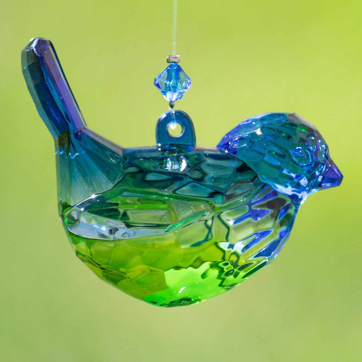 Close-up of a faceted blue-green bird ornament hanging from a clear thread.