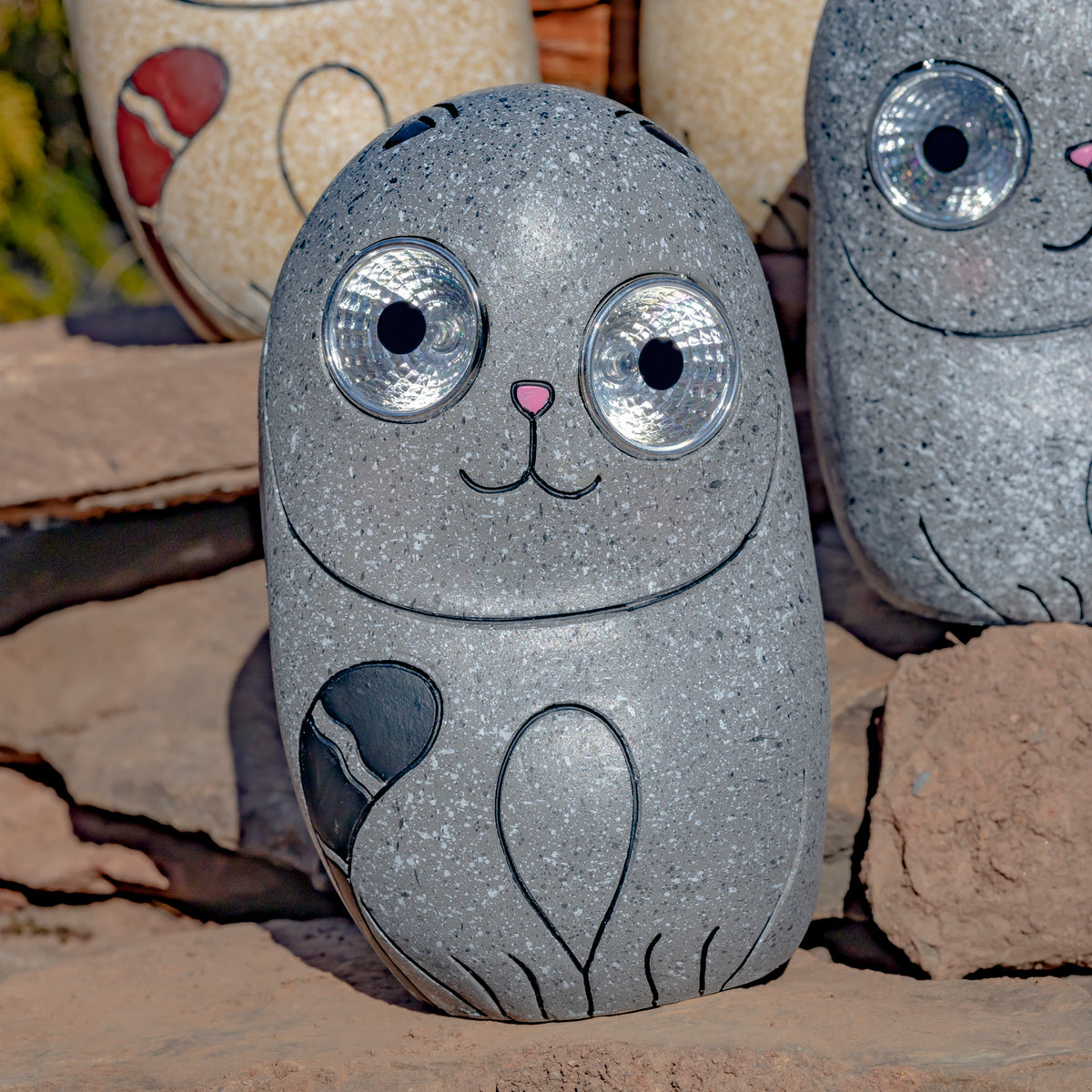 Close-up of a speckled gray cat ornament showing its reflective round eyes and outlined paws.