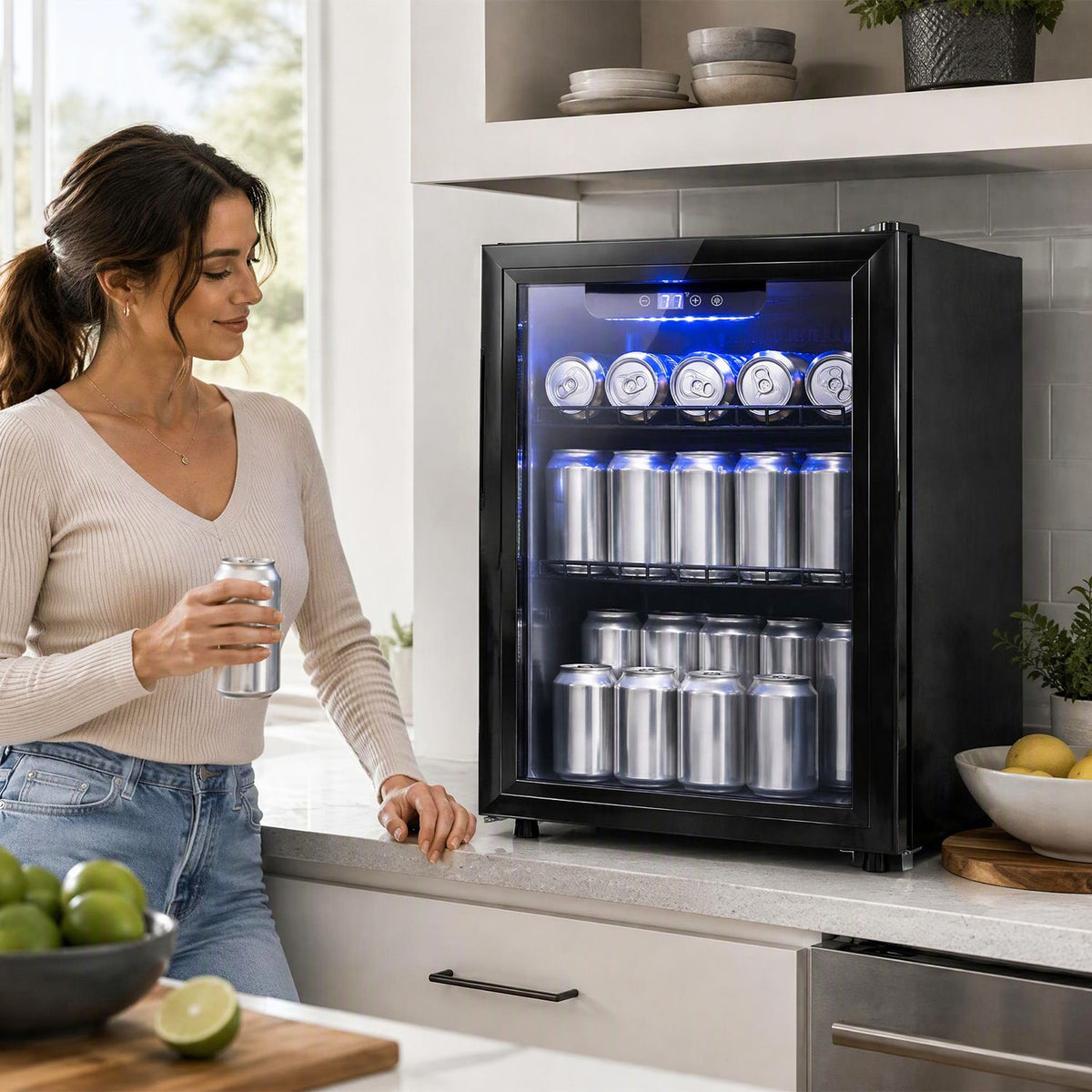 Black glass-door beverage refrigerator glowing blue on a kitchen counter beside a woman holding a drink.