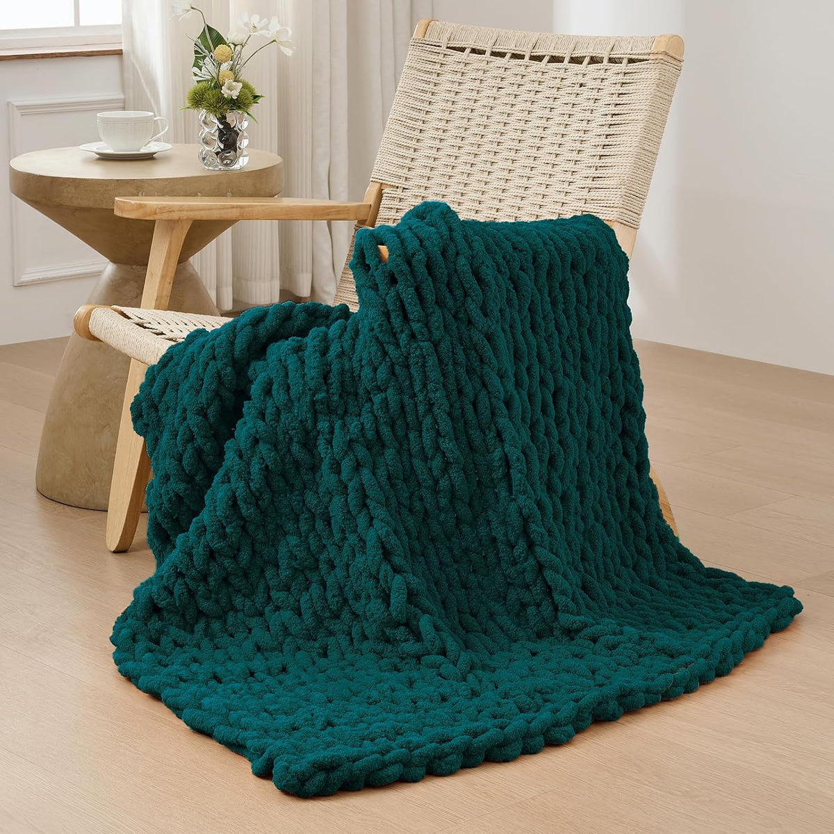 Deep teal chunky knit throw draped over a woven wooden chair, pooling onto the floor