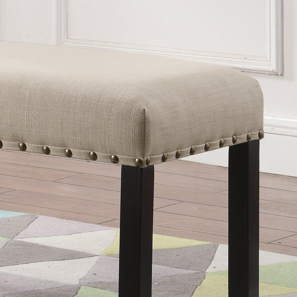 Detail close-up of tan fabric seat corner with brass nailhead trim and black leg on hardwood floor