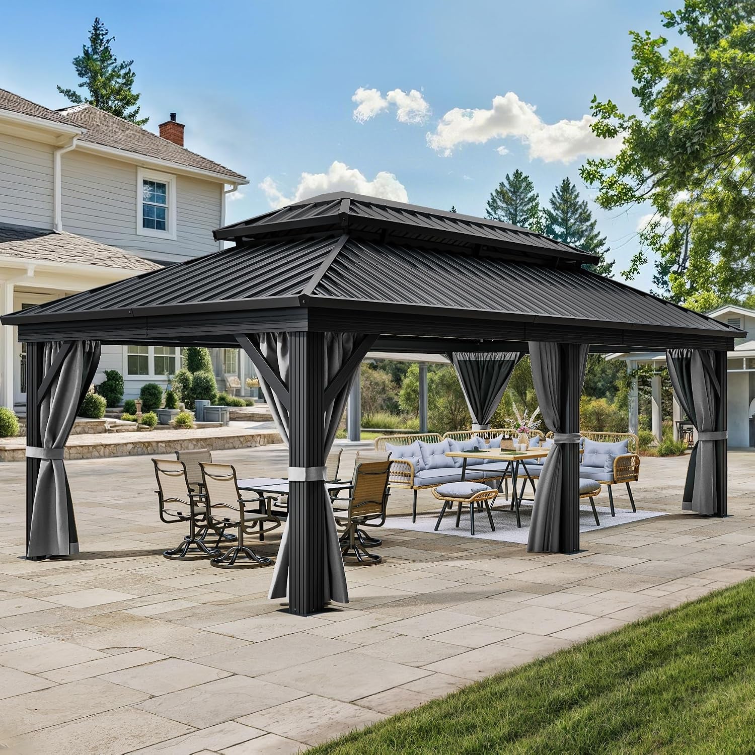 Three-quarter view of a gray hardtop gazebo on a stone patio with tied curtains and dining seating, house in background.