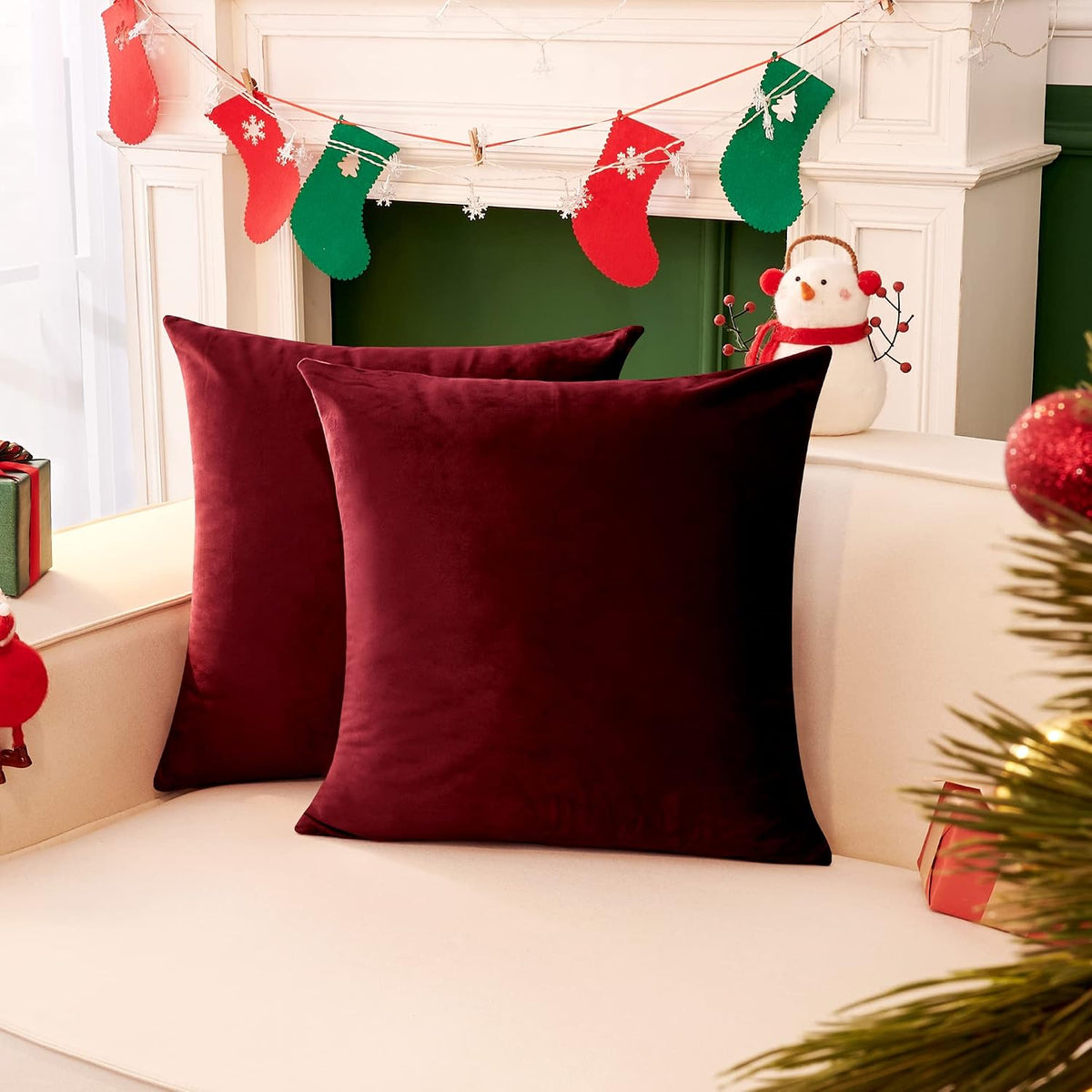Two deep burgundy square pillow covers on a sofa with holiday stockings and a snowman decoration