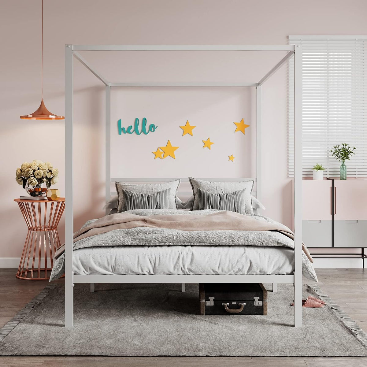 Front view of the white metal canopy bed staged in a pink bedroom with pillows and side table.