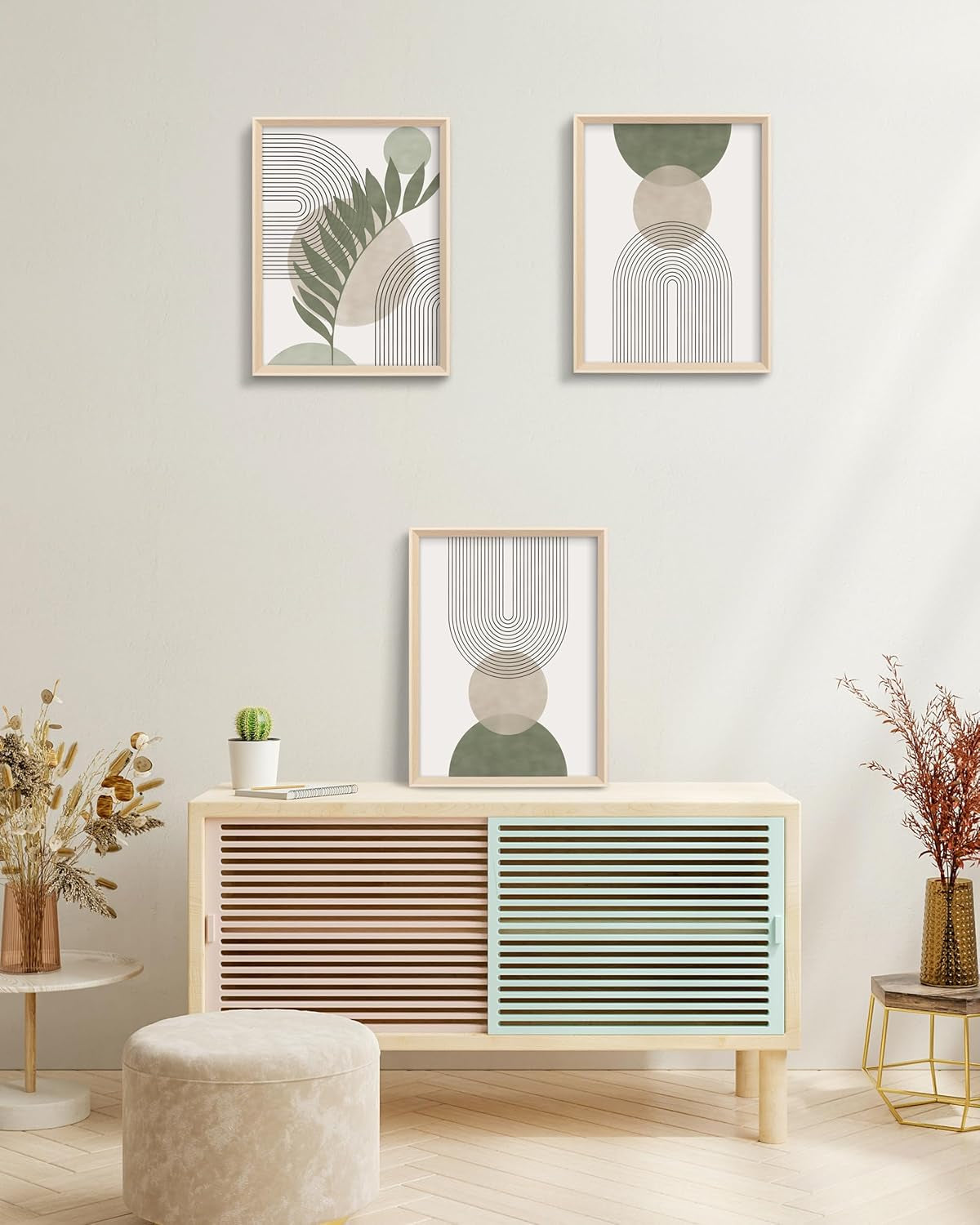 Three sage and neutral framed prints displayed as a gallery above a wooden console in a neutral living space