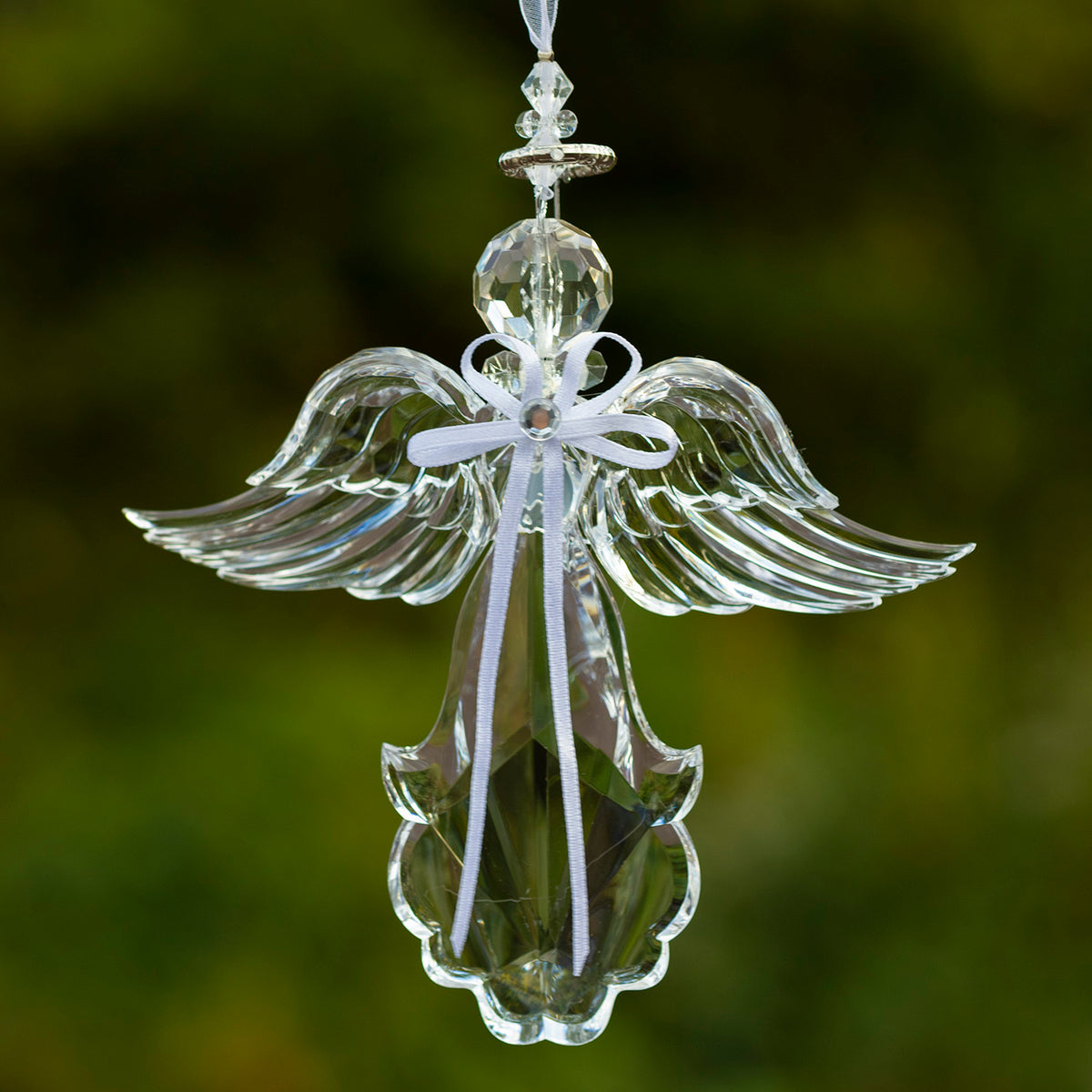 Clear hanging angel ornament with wide curved wings, a white ribbon bow, and faceted details against a green background.