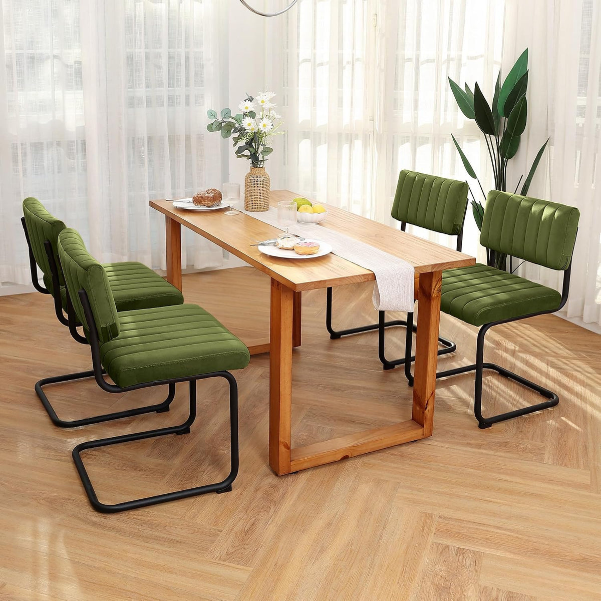 Set of four olive green velvet cantilever chairs paired with a wooden dining table in sunlit room
