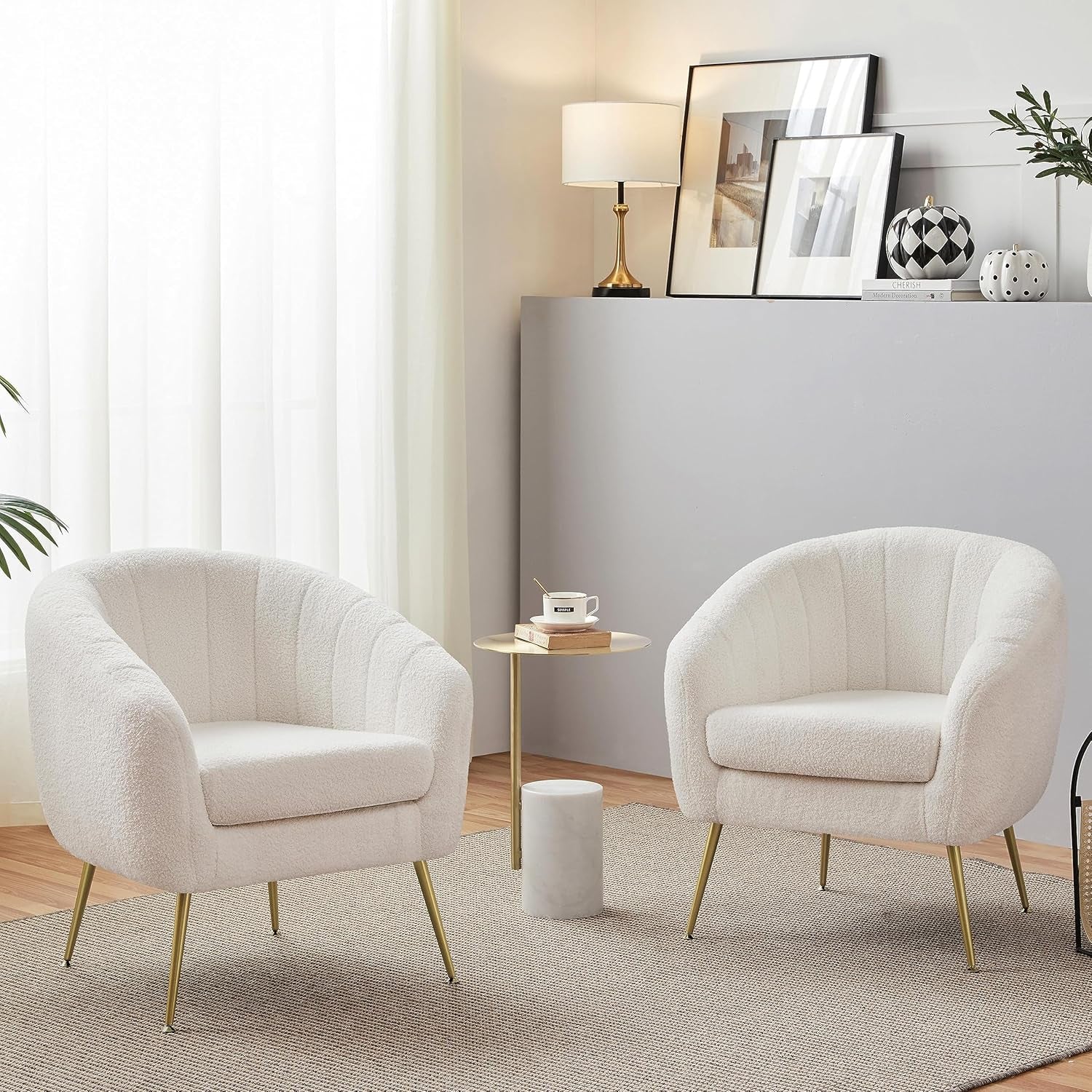 Room scene with two ivory bouclé barrel chairs with gold tapered legs beside a small round side table.