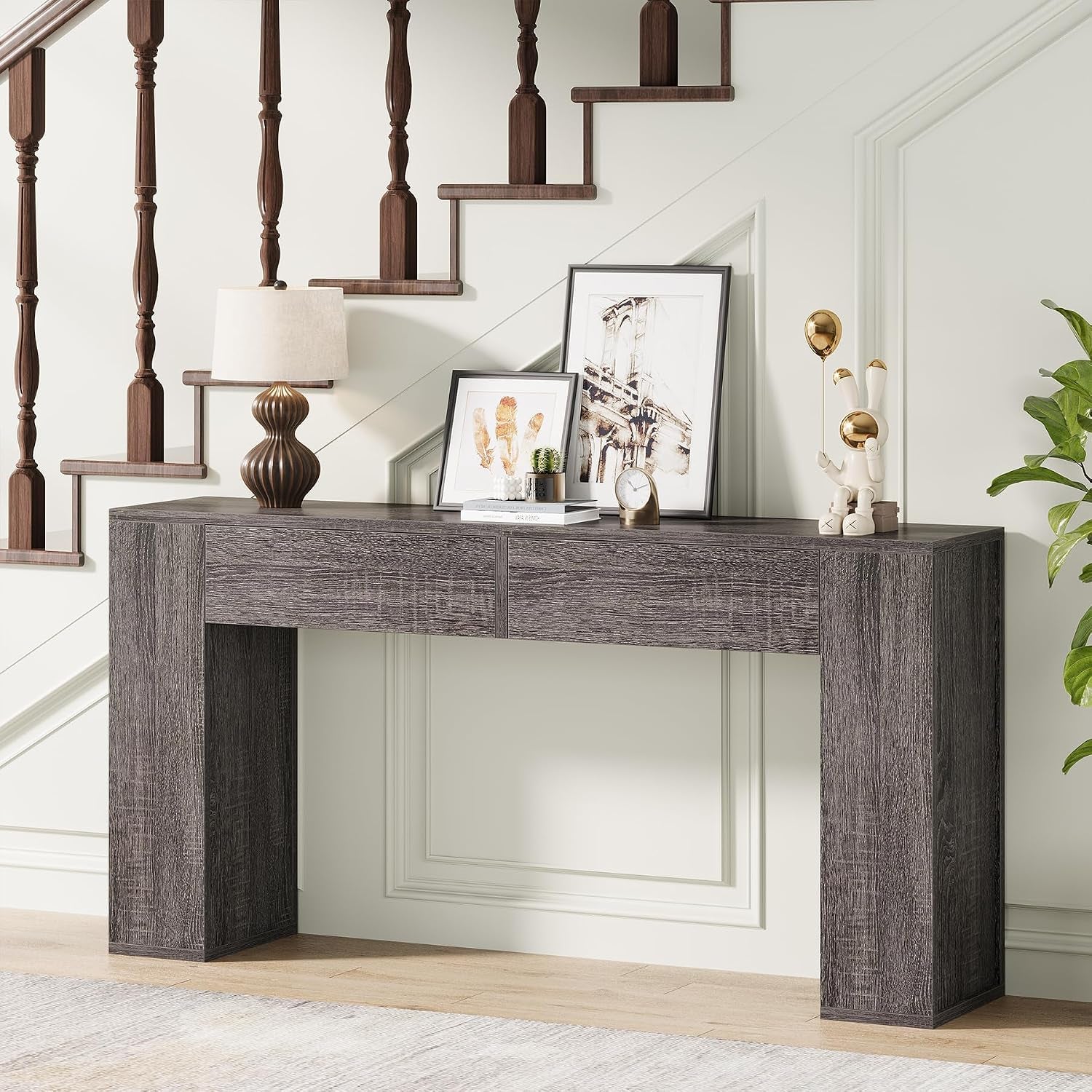 Console table in a staircase nook decorated with a table lamp, leaning artwork and small accessories.