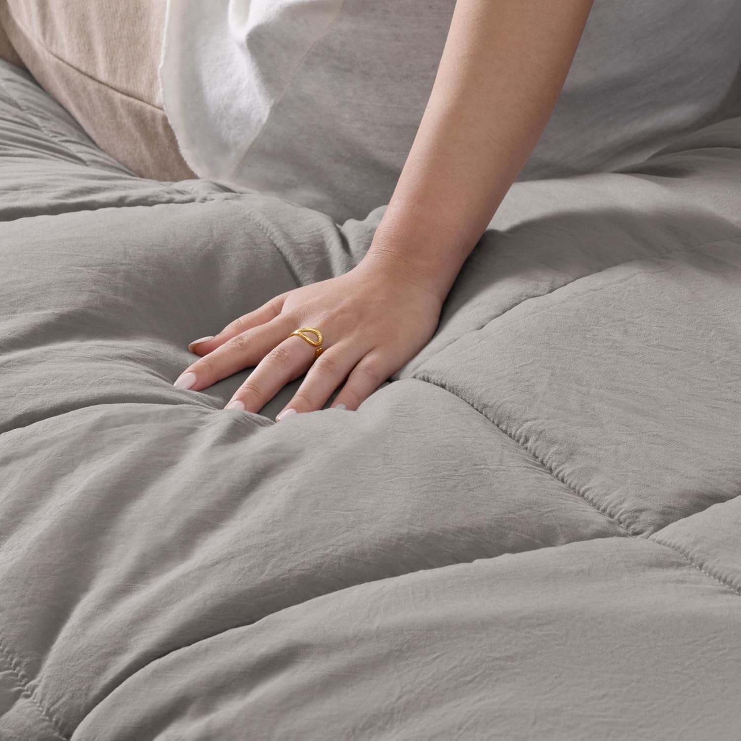 Close-up of a hand pressing into the quilted comforter to show soft loft and stitching.