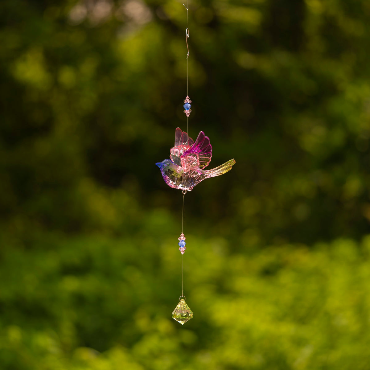 A pink-accented acrylic bird hangs on a fine strand above beads and a green faceted drop.