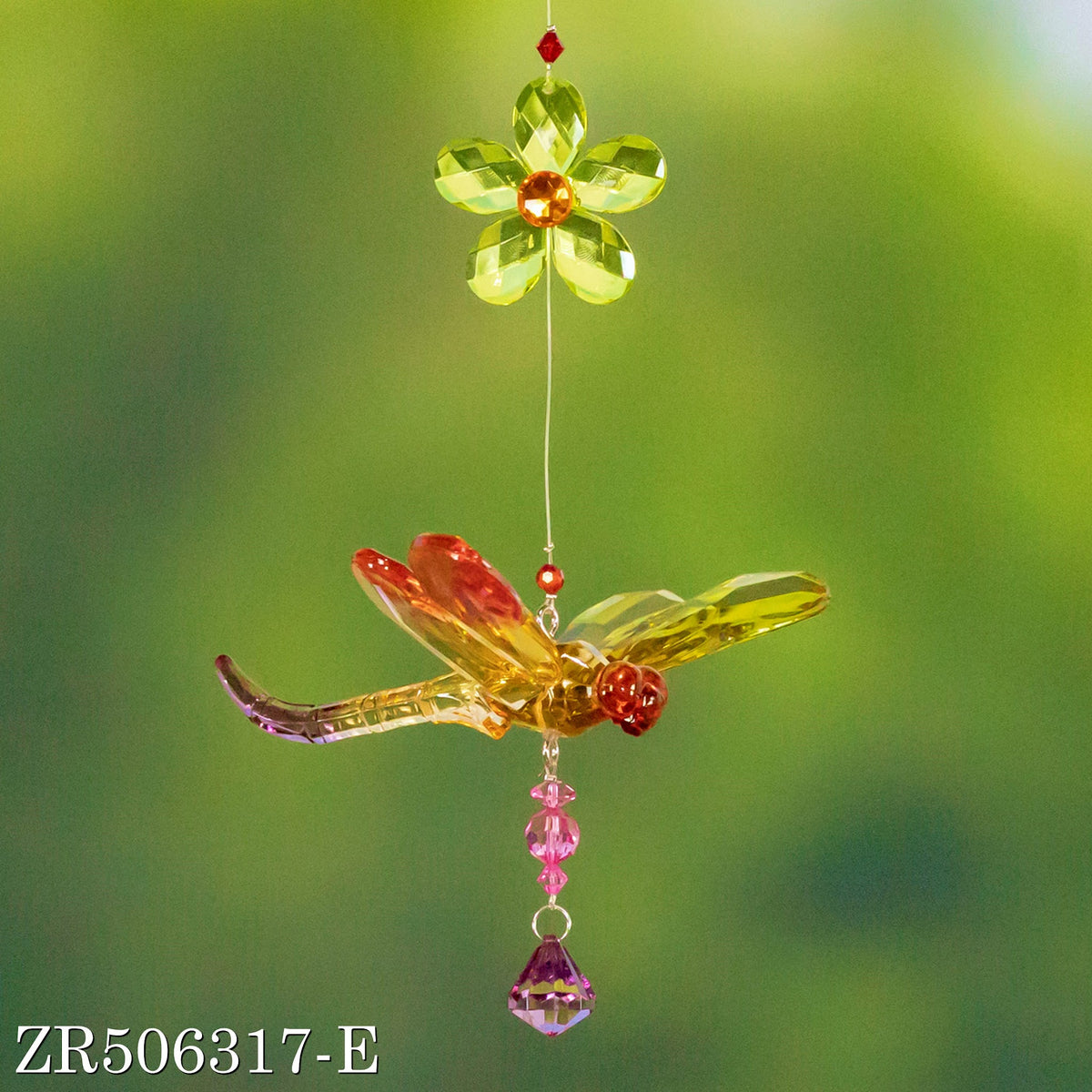 A faceted multicolor dragonfly ornament hangs beneath a green flower against a blurred background.