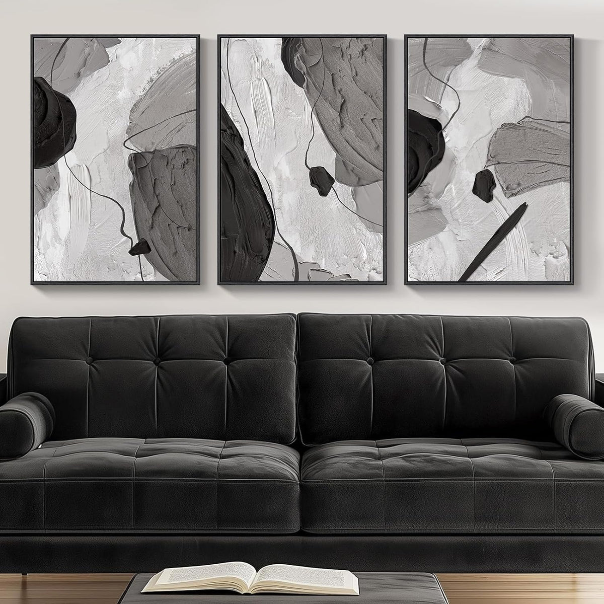 Three monochrome gray abstract panels hung above a tufted black sofa with an open book on the coffee table in front.
