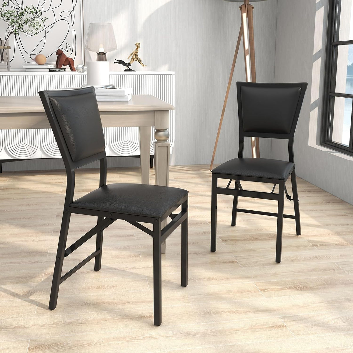 Two black folding dining chairs staged near a light wood dining table on a herringbone floor
