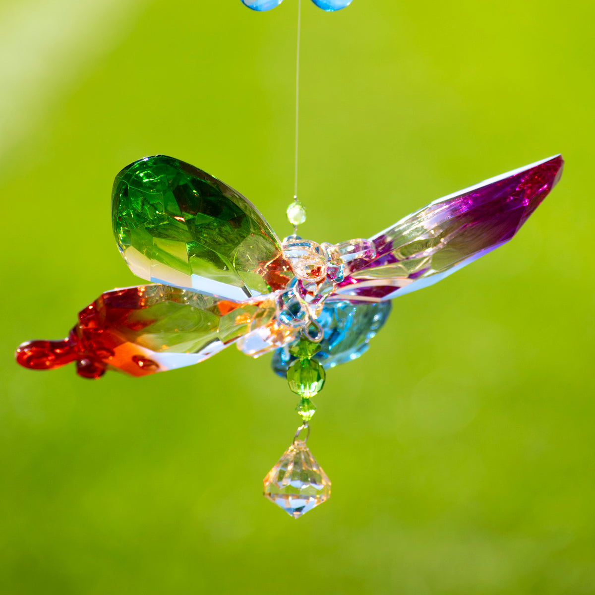 Colorful faceted butterfly ornament hanging against a bright green background, with a dangling crystal drop.