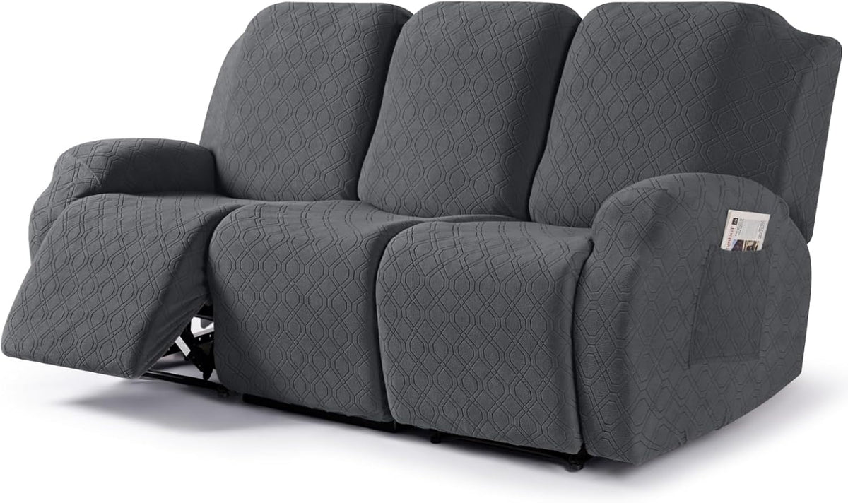 Dark gray stretch cover fitted on a three-seat recliner, left footrest extended, side pocket holding a magazine.