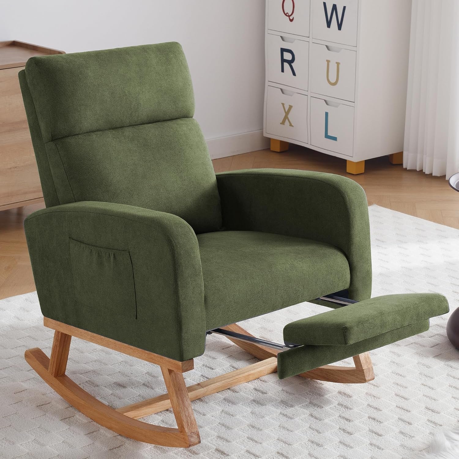 Olive green rocking chair with light wood base and extended footrest beside a toy storage unit.