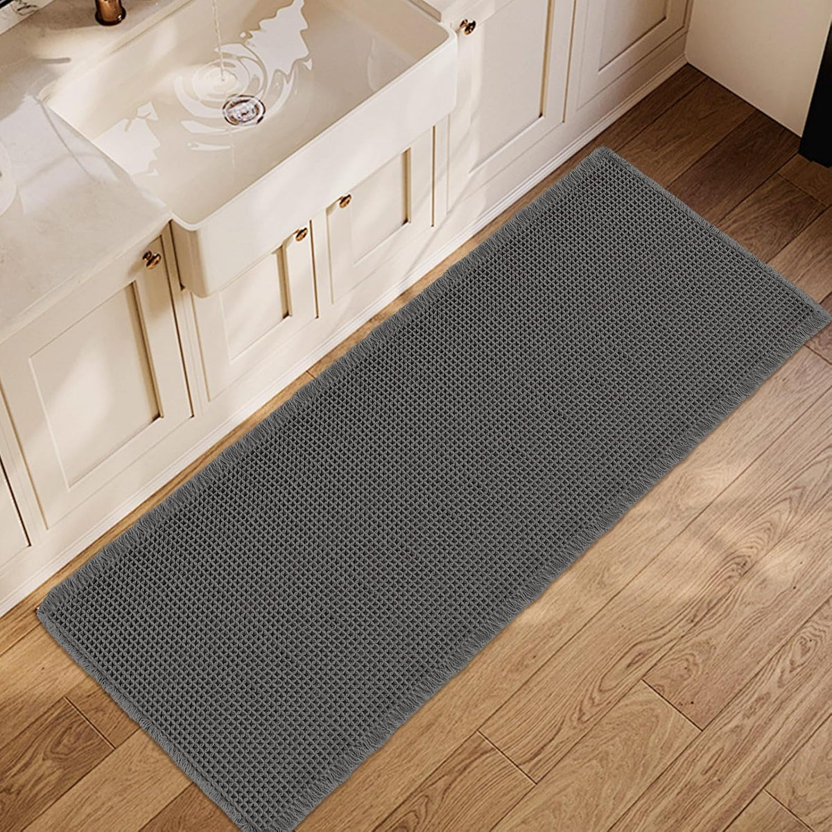 Rectangular waffle bath mat in dark charcoal gray placed on wood floor in front of a sink cabinet.