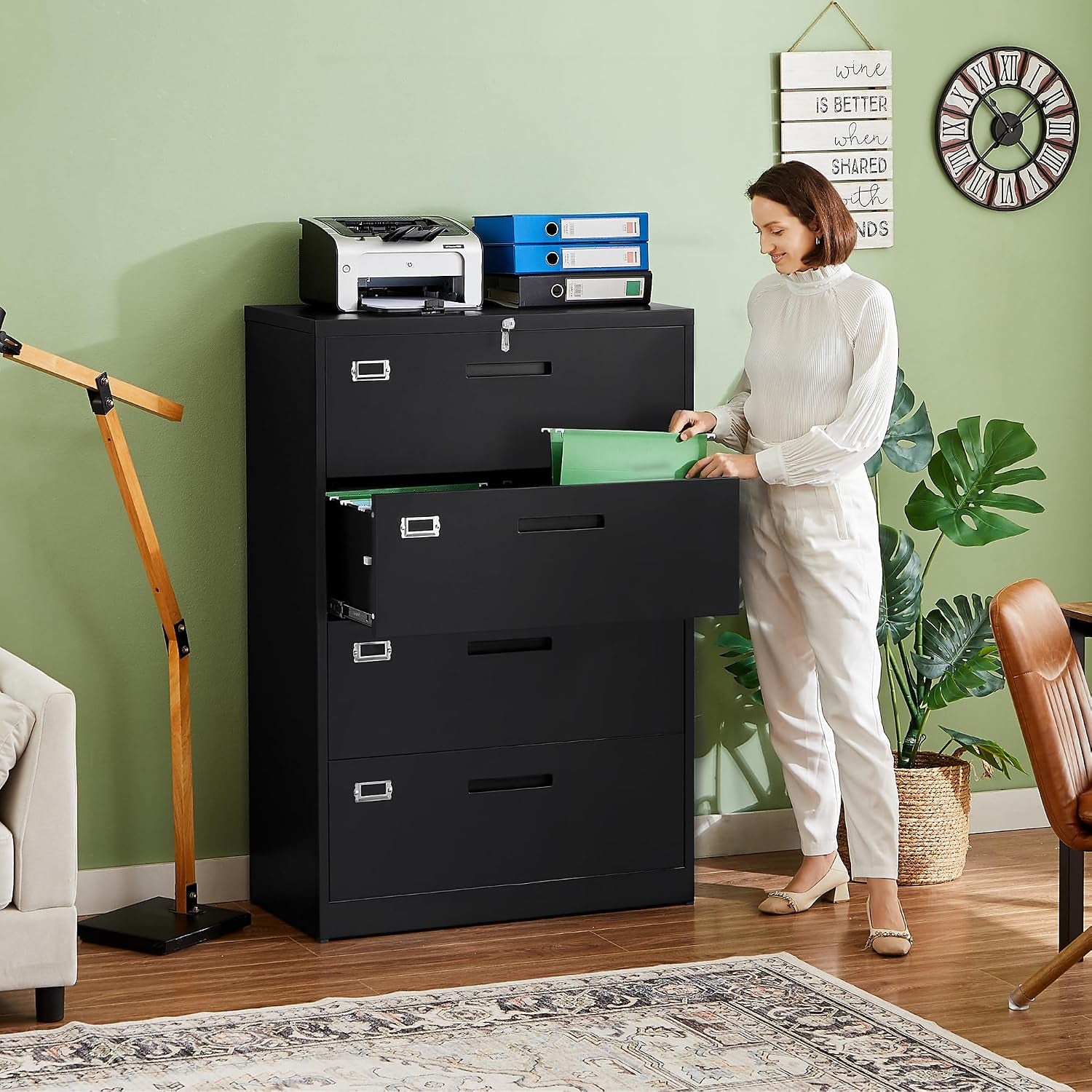 Woman standing in a home office next to a black four-drawer file cabinet, opening a middle drawer.