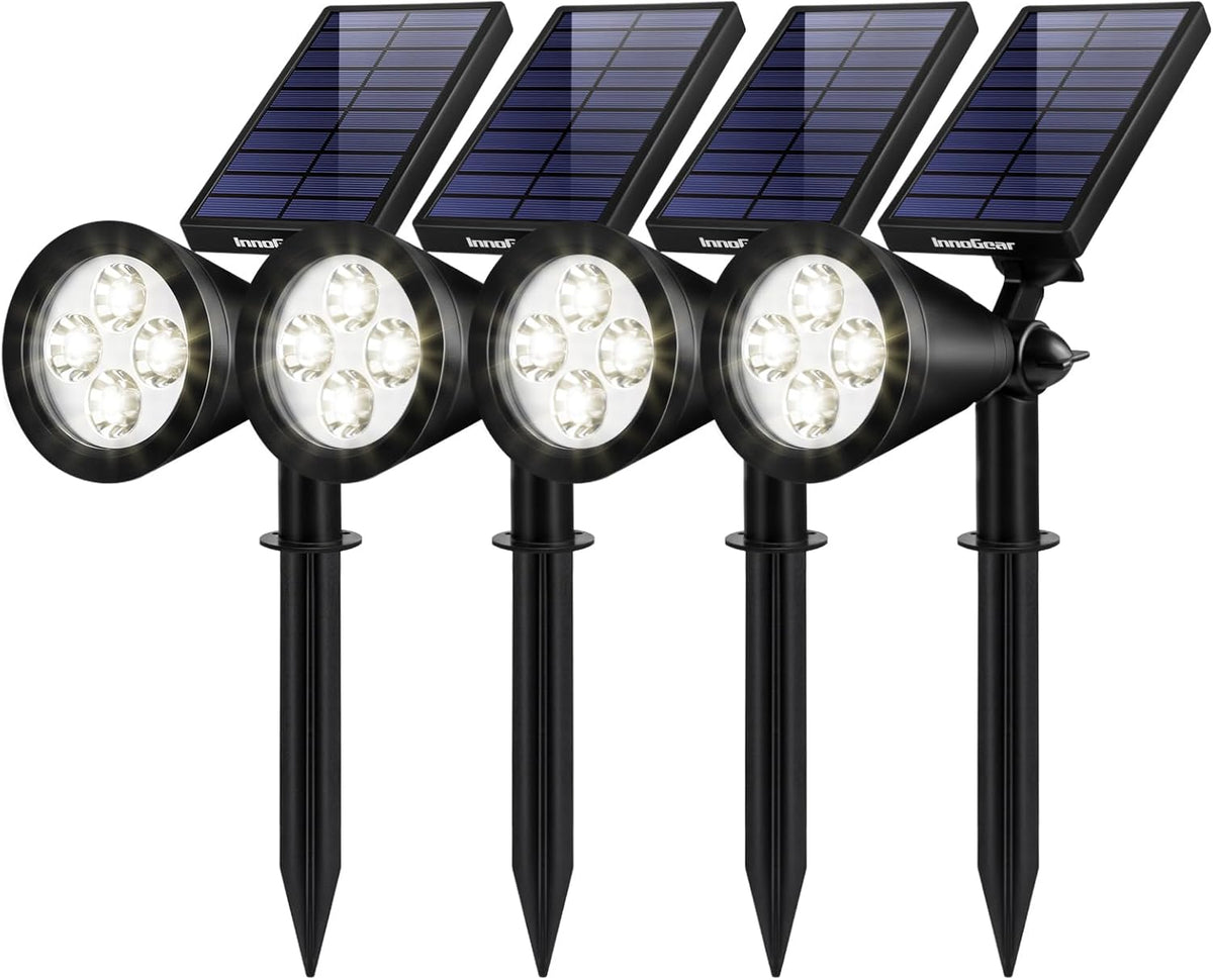 Four black solar landscape spotlights in a row, each with a rectangular solar panel and four LED bulbs lit.
