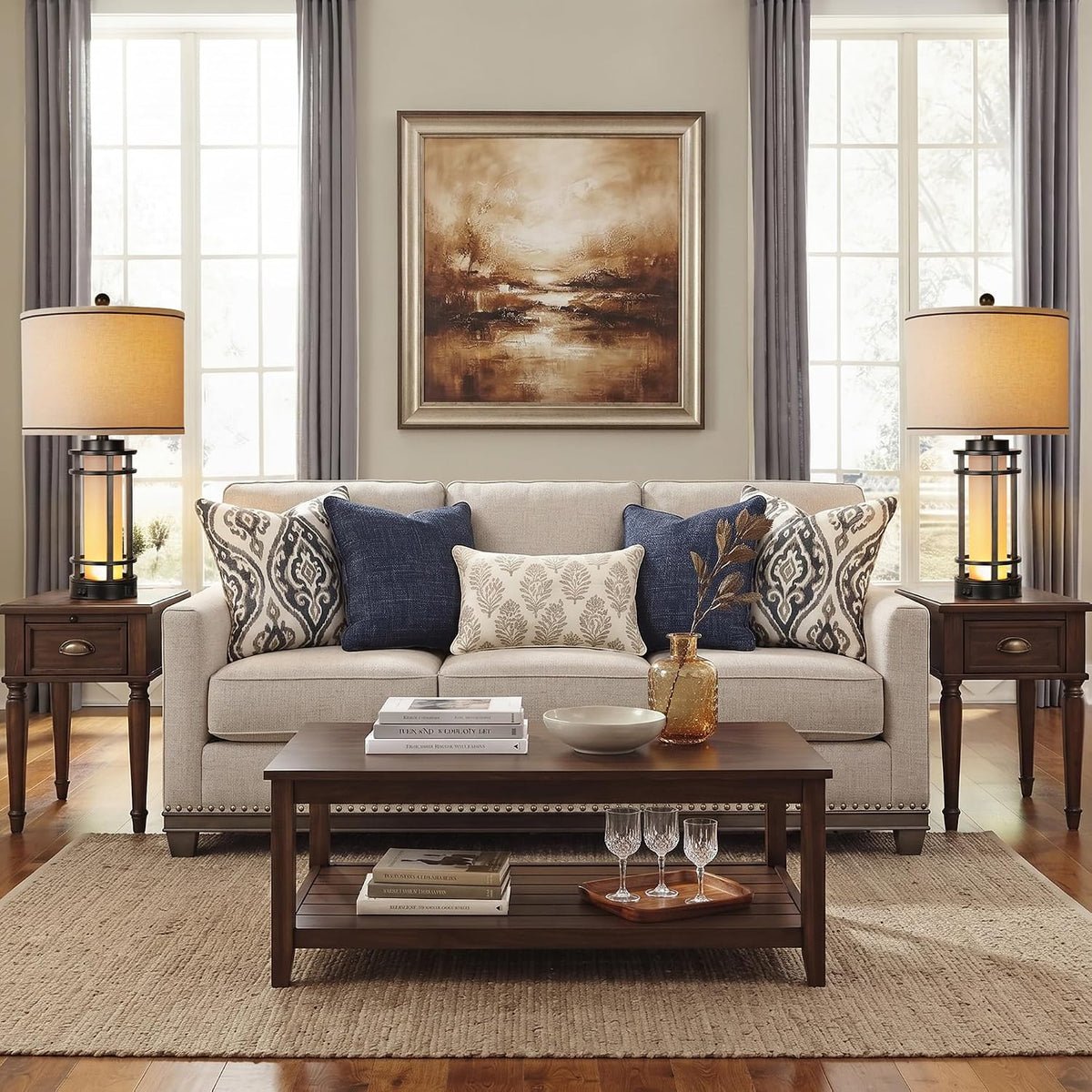 Front living-room view with two lit table lamps on matching side tables flanking a sofa and centered painting