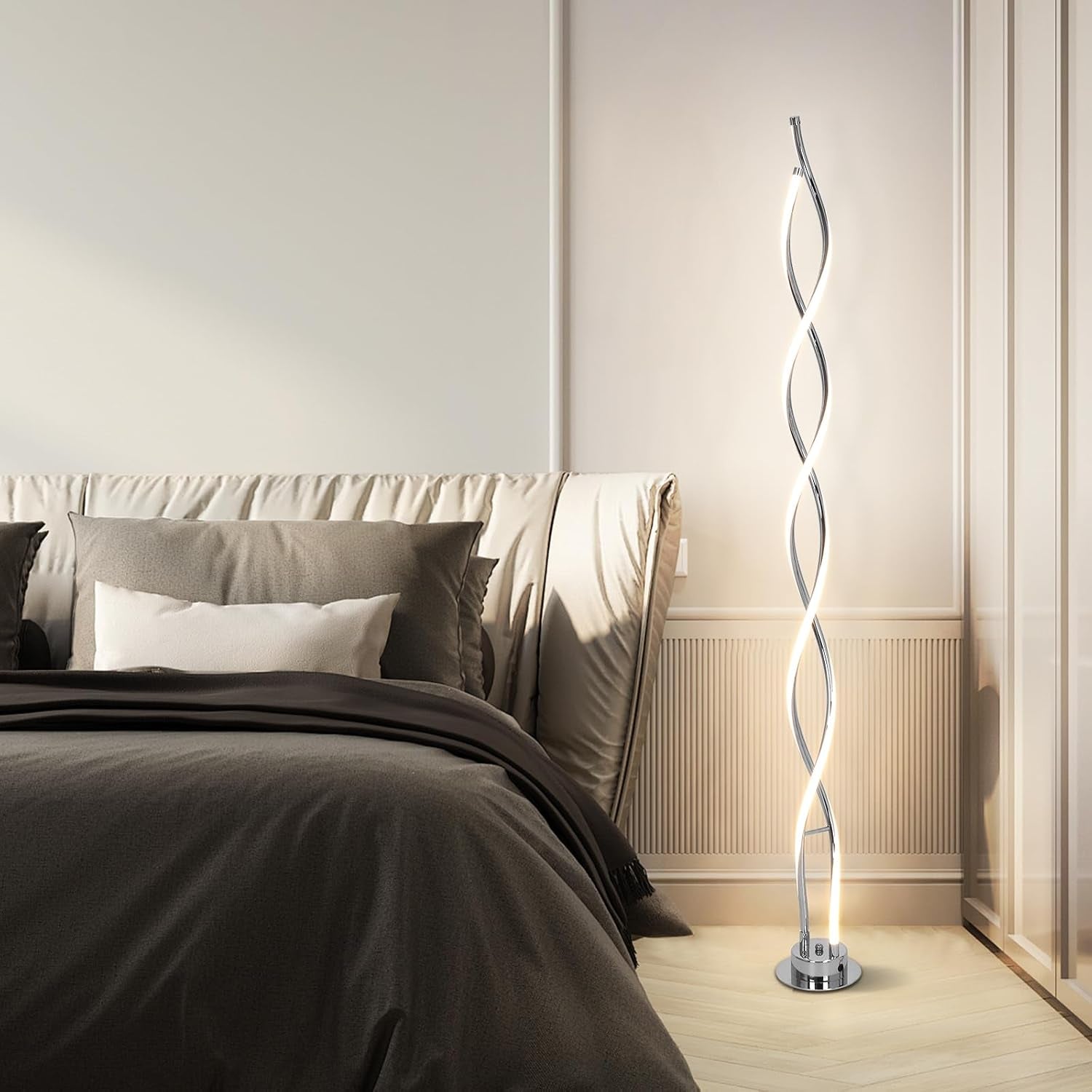 Bedroom scene showing a made bed and a spiral LED floor lamp lit on the floor next to the headboard.