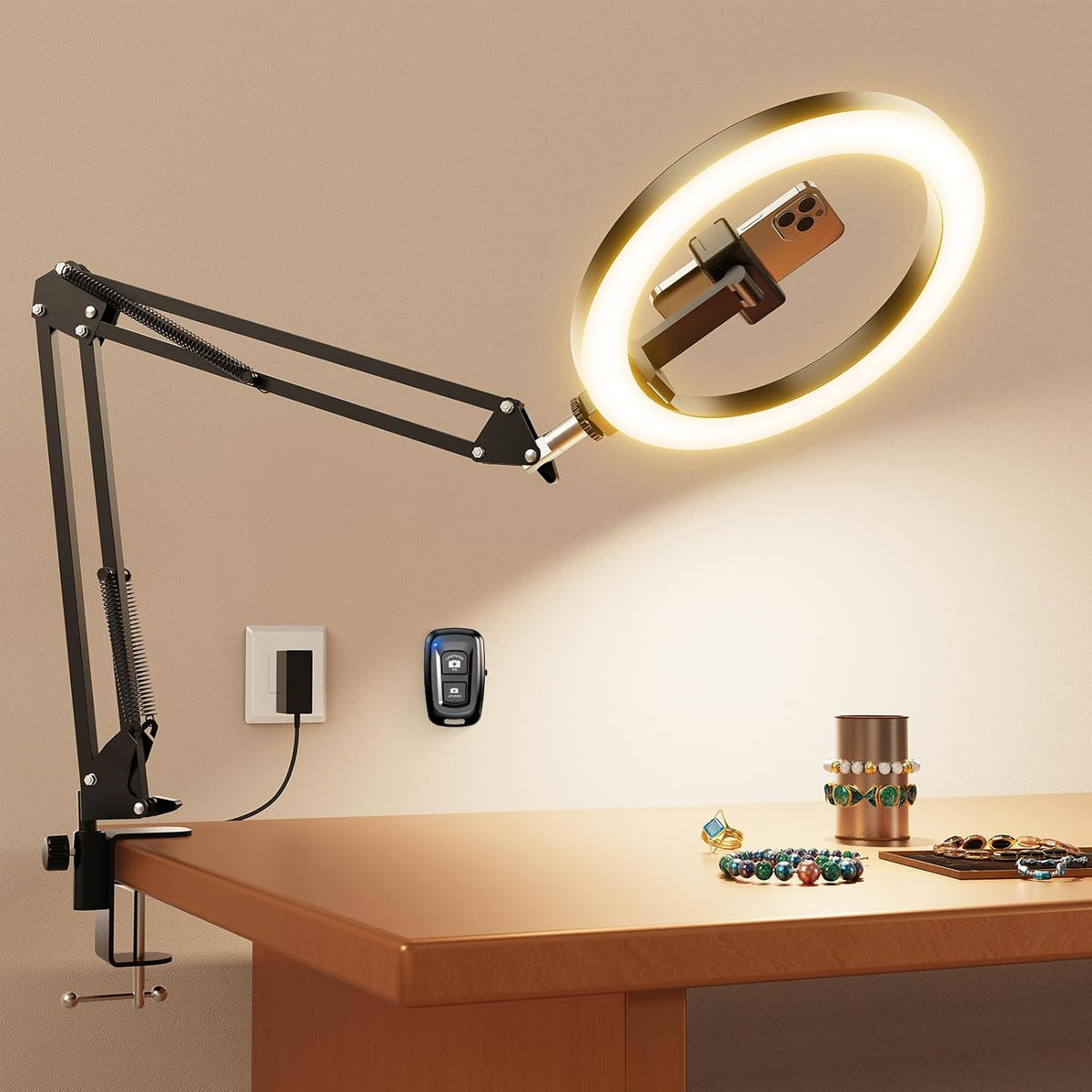 Lit ring light angled over a desk with jewelry below, showing the clamp, power cord, and wall remote
