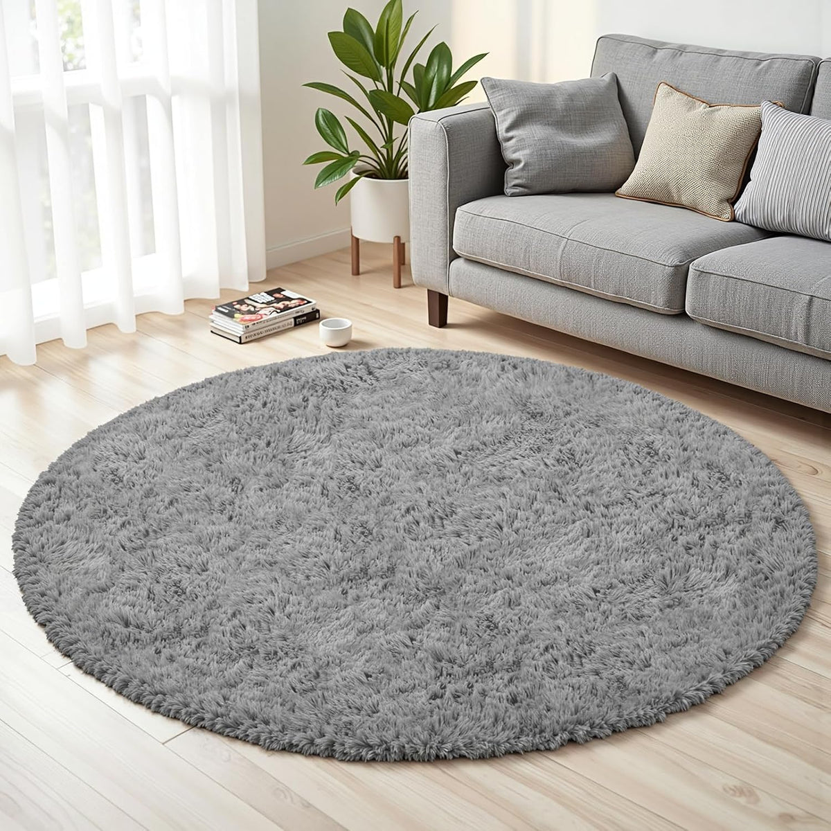 Side view of a round light gray shag rug on a light wood floor next to a gray sofa and potted plant.