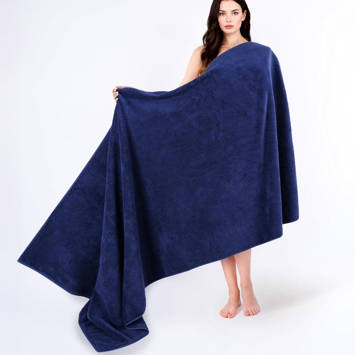Woman wrapped in an oversized deep navy bath towel, holding one edge out to show size.