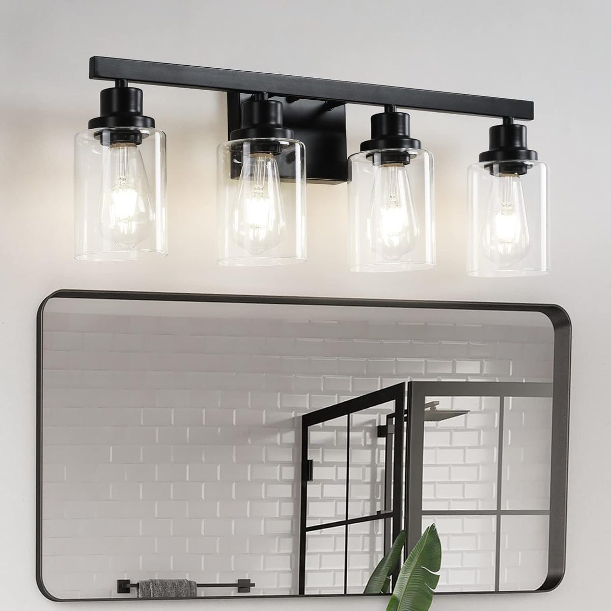 Four-light black vanity fixture with clear glass shades reflected in a mirror above a bathroom sink