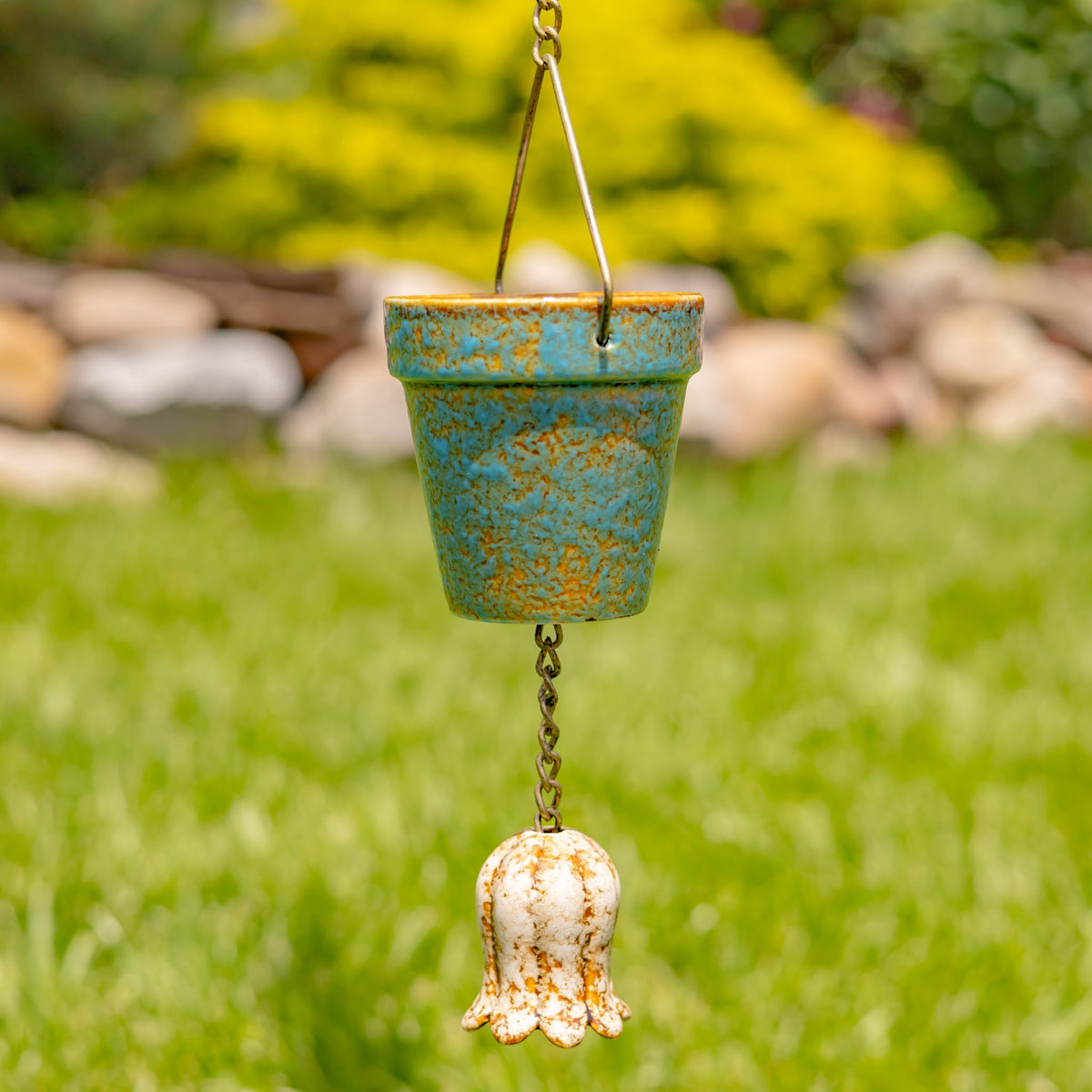 A turquoise and brown pot hangs outdoors above a cream-colored, flower-shaped ornament.
