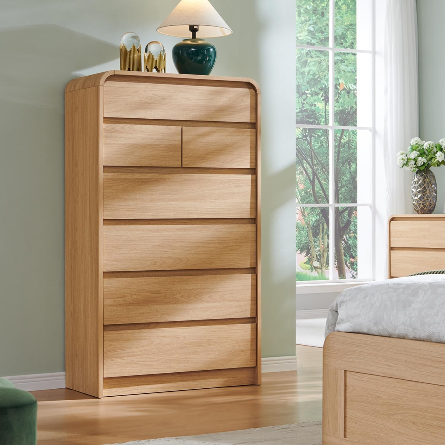 Natural oak tall dresser in staged bedroom beside bed with window in background