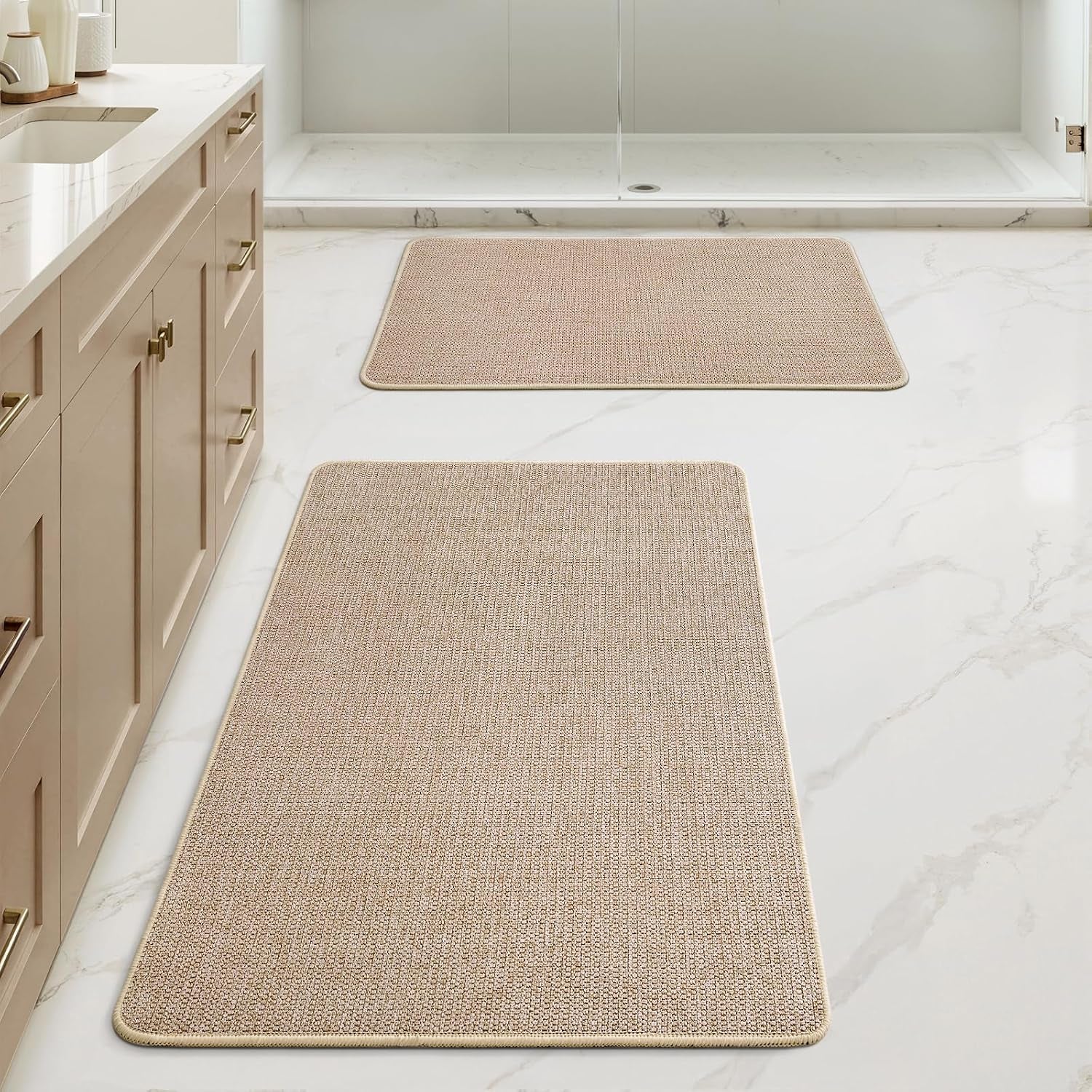 Bathroom scene showing two beige rugs, closer view emphasizing texture and placement.