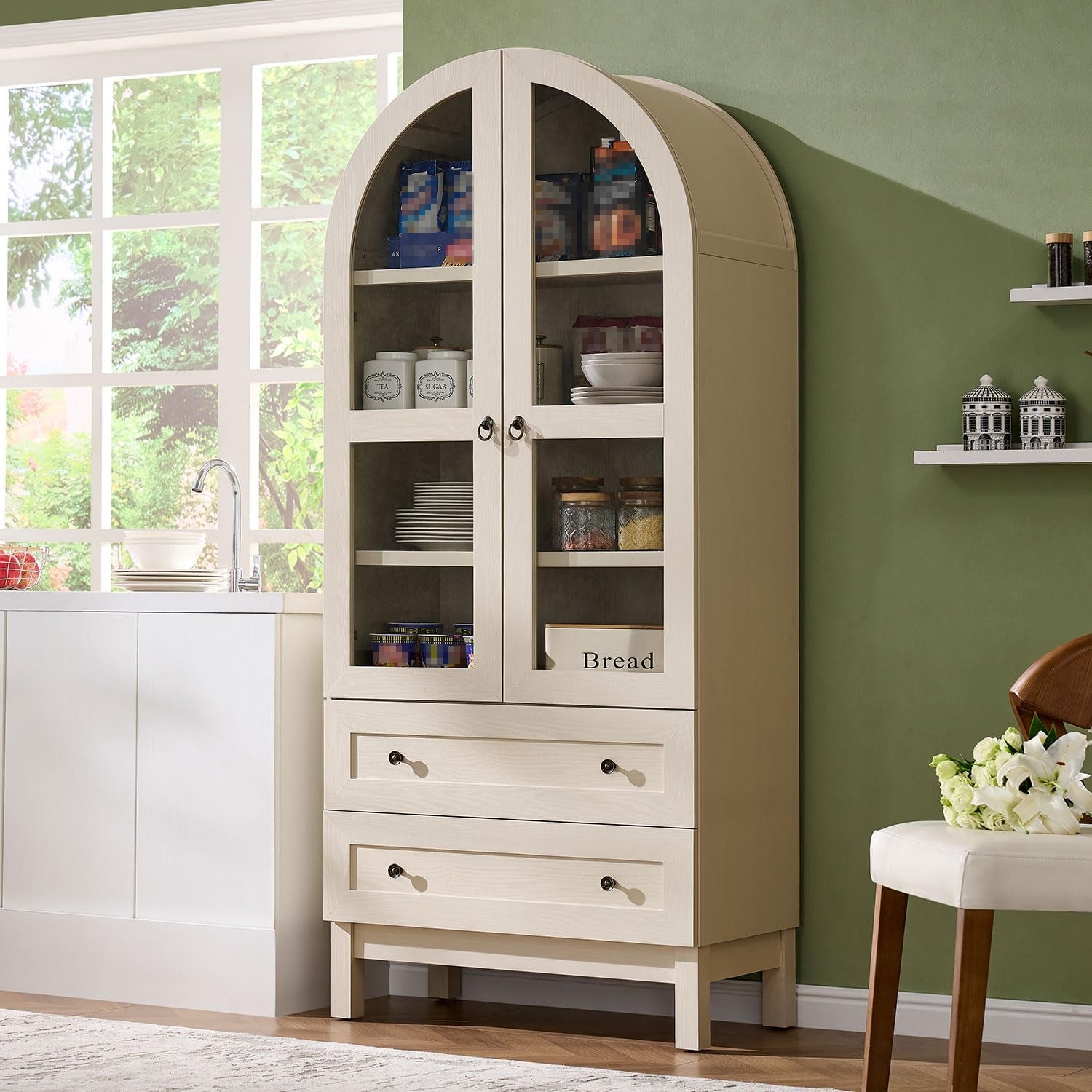 Light-finish arched pantry with glass doors and two drawers beside a sink and a green painted wall.