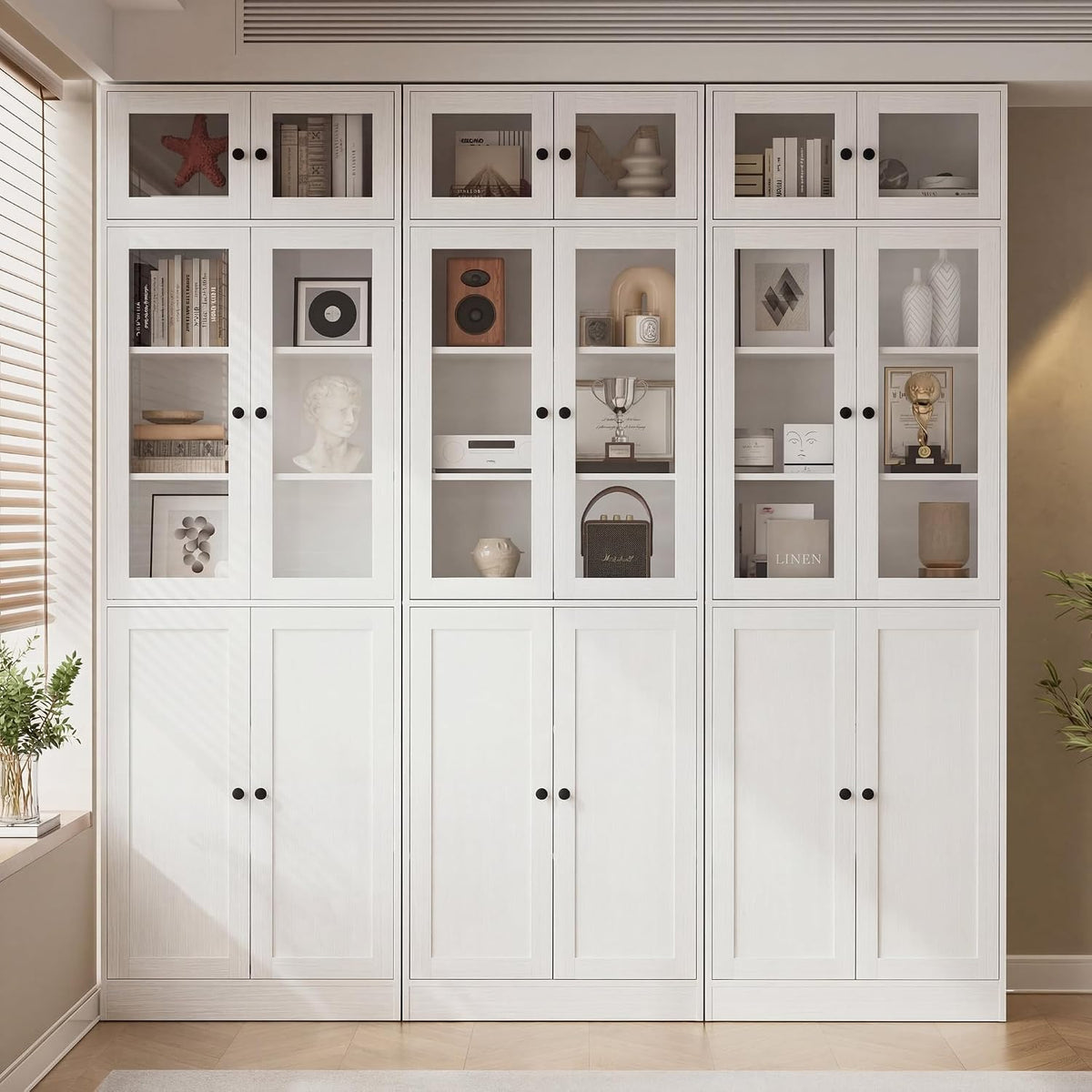 Three white bookcase modules side-by-side with glass upper doors and closed lower doors filled with decor.