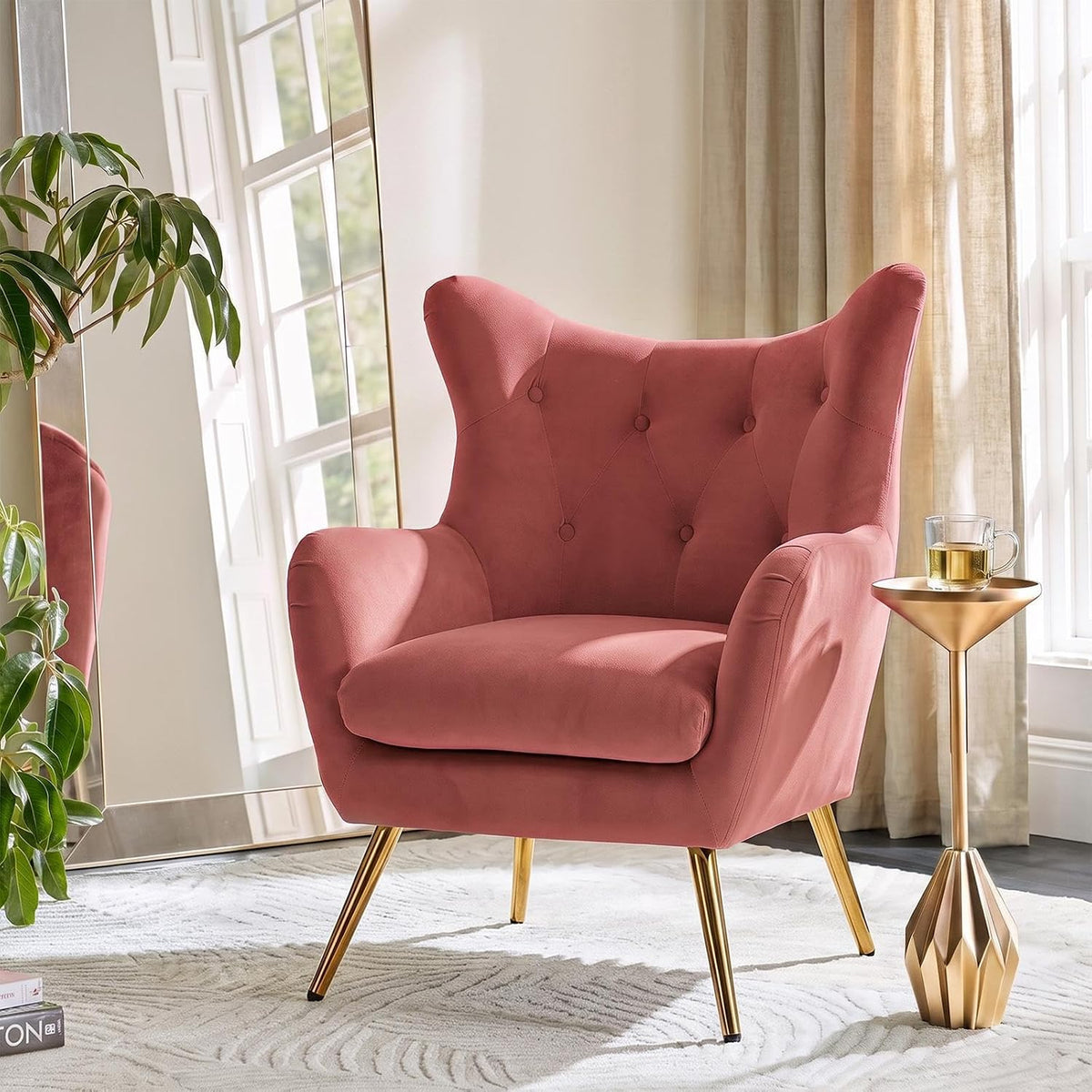 Rose‑colored velvet wingback chair with button tufting and gold legs beside a small gold side table.
