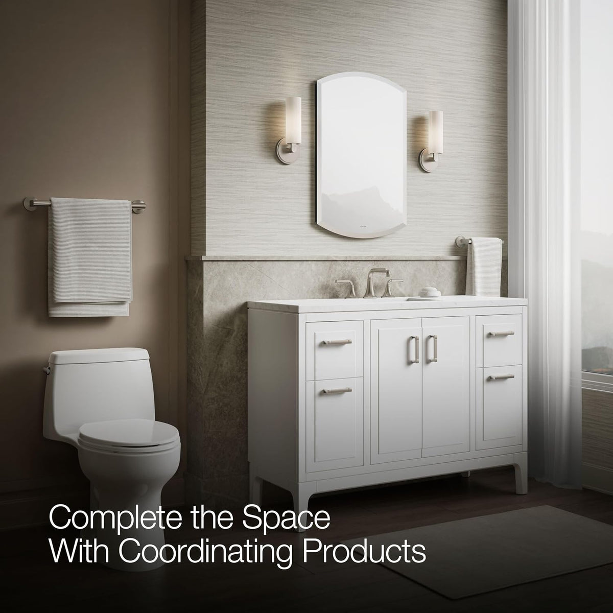 Wide view of a neutral bathroom with arched mirror above white vanity, toilet at left and window with sheer curtain at right