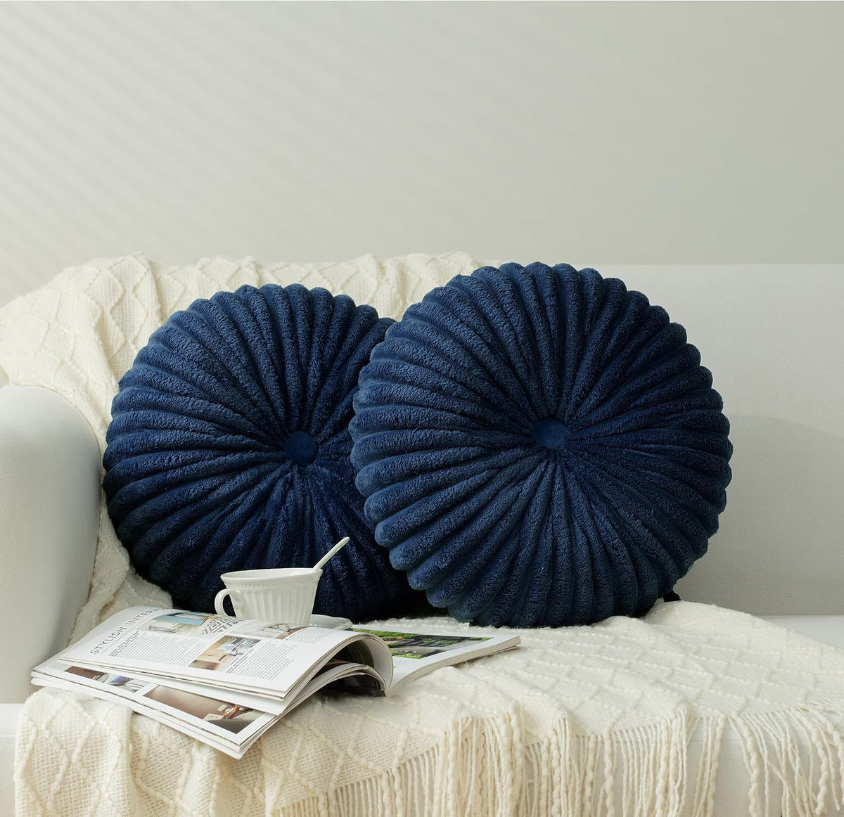Two round ruched navy blue pillows with button centers on a cream knit throw and sofa.