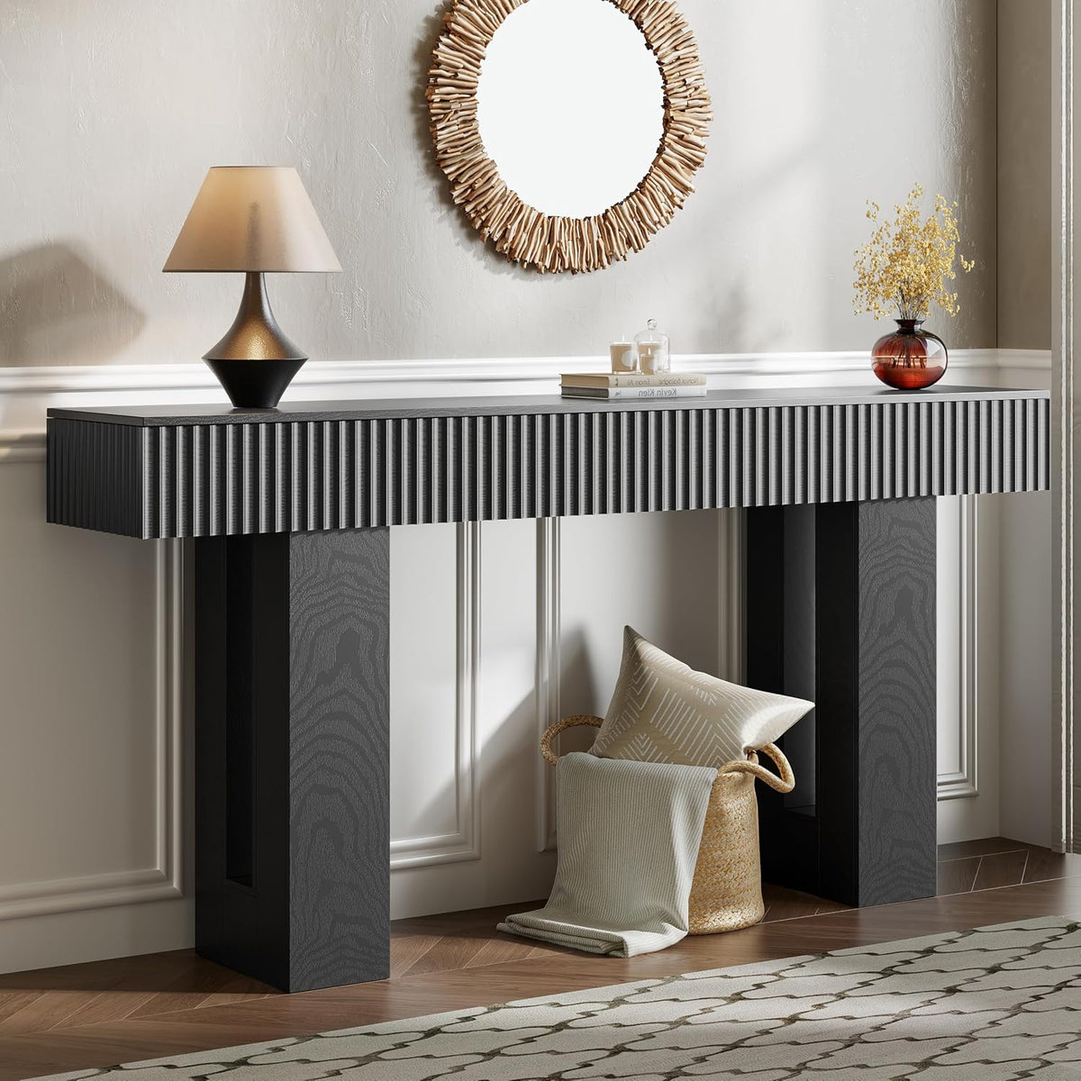 Dark charcoal fluted console table in a foyer with a lamp, round driftwood mirror and basket of pillows below