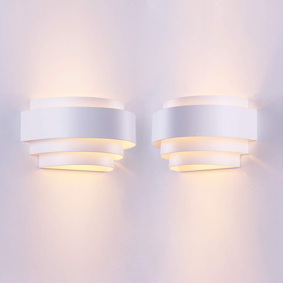 Pair of white layered half‑moon wall sconces mounted side by side, casting warm up-and-down light.