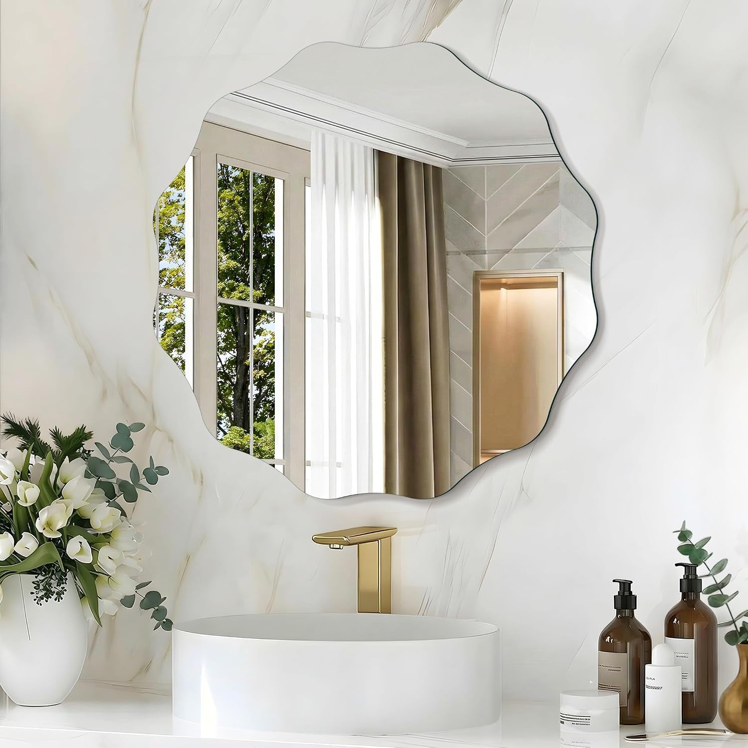 Scalloped mirror above a round vessel sink with a gold faucet, toiletries and a vase of white flowers.