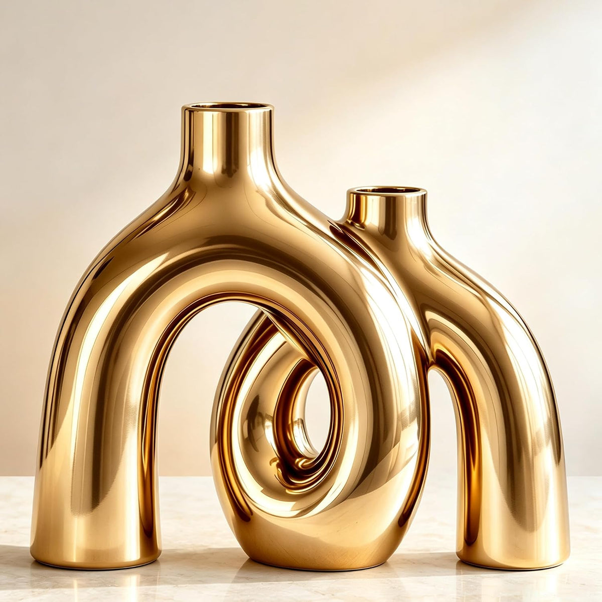Glossy reflective gold pair of interlocking donut-shaped ceramic vases on a light surface.