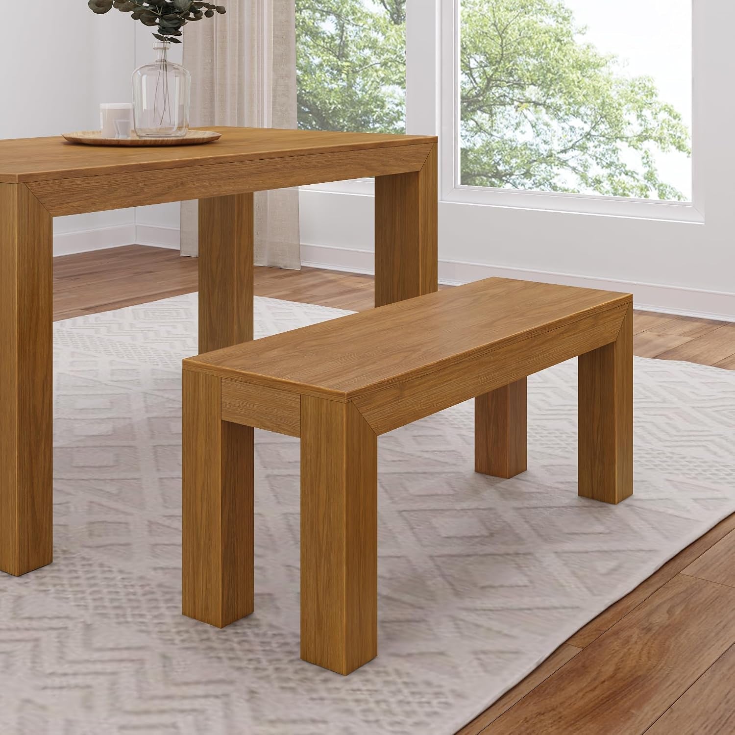 Corner view of a rectangular pine dining table and matching bench with warm medium wood tone on a patterned rug.