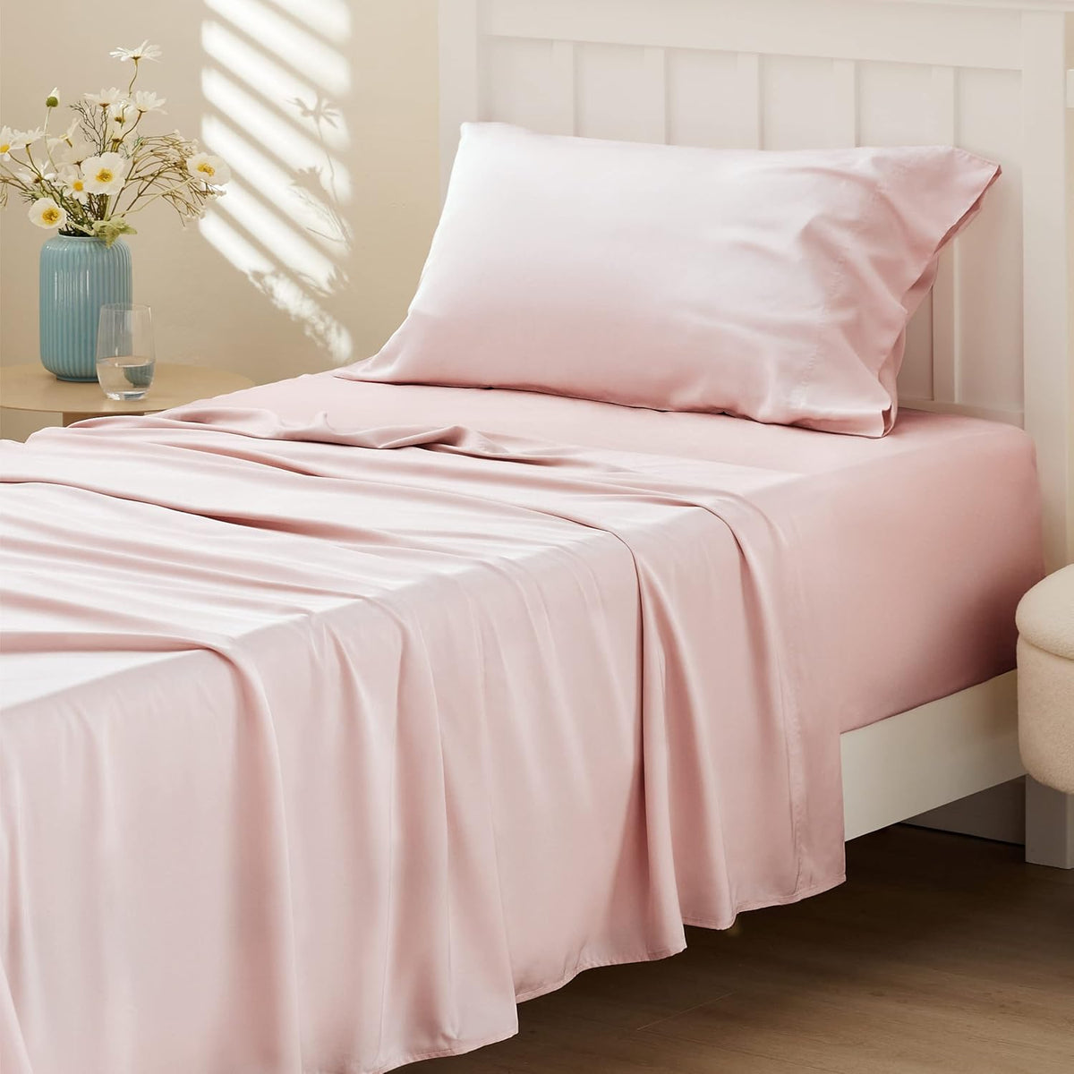 Close corner view of a bed with soft blush pink sheets and a matching pillow against a white headboard